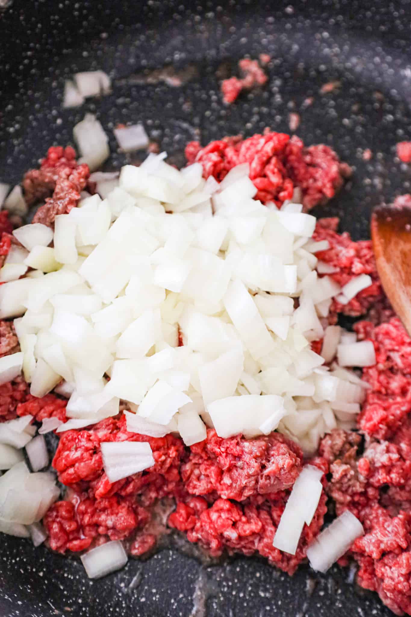raw ground beef and diced onions in a saute pan