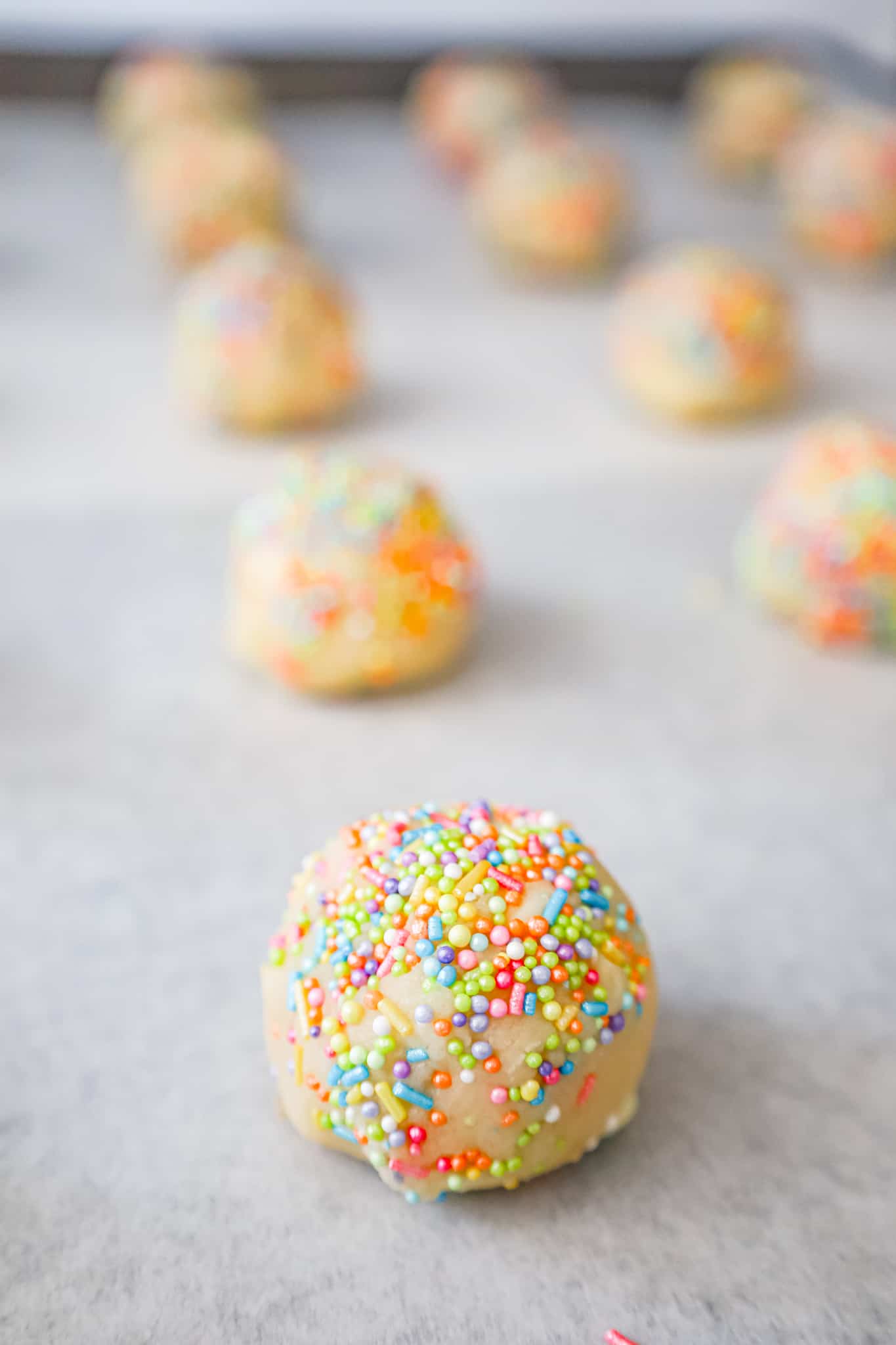 rainbow sprinkle covered cookie dough ball on a parchment lined baking sheet