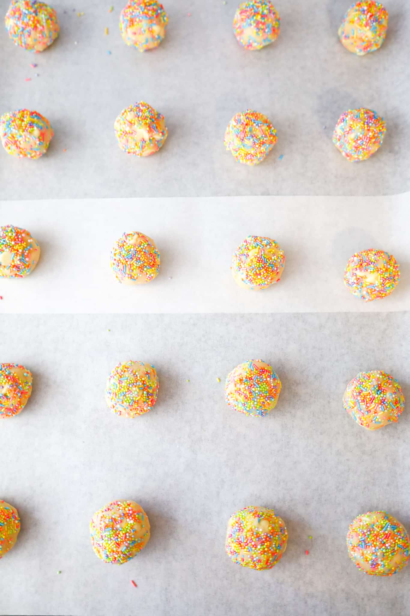 cookie dough balls coated in rainbow sprinkles on a parchment lined baking sheet