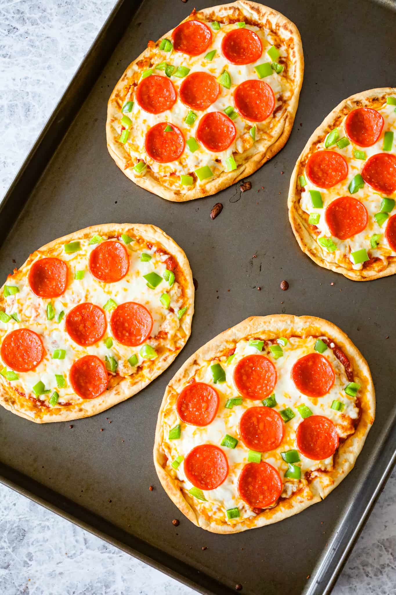 Naan Pizza is an easy dinner recipe using store bought naan bread topped with pizza sauce, shredded mozzarella cheese, sliced pepperoni and diced green peppers.