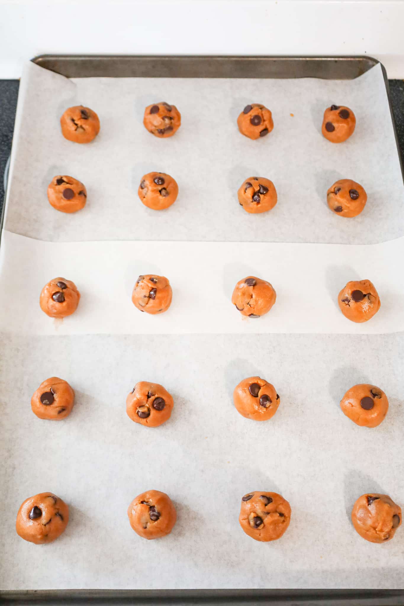 peanut butter chocolate chip cookie dough balls on a parchment lined baking sheet