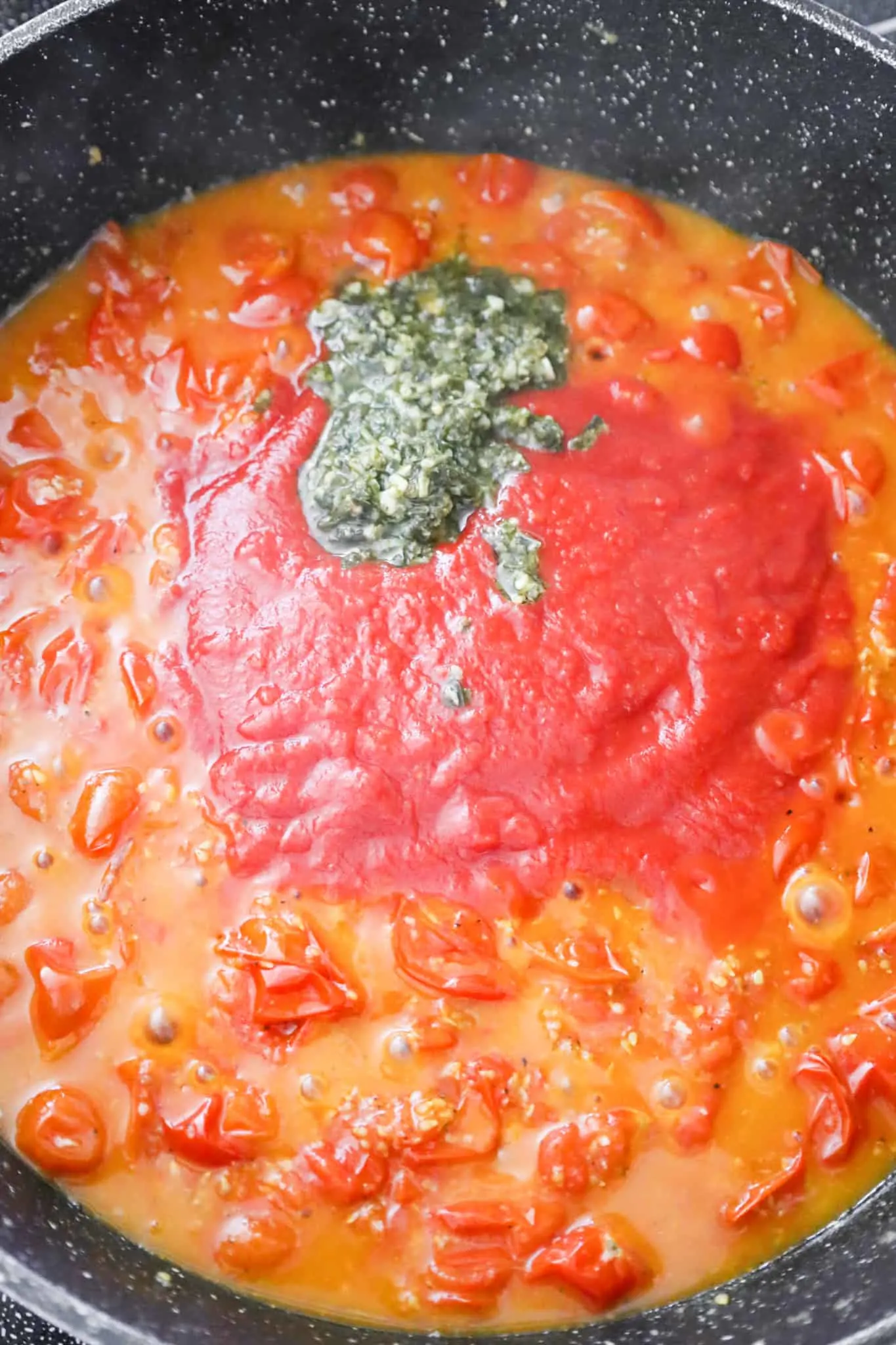 basil pesto and crushed tomatoes on top of cooked cherry tomatoes in a saute pan