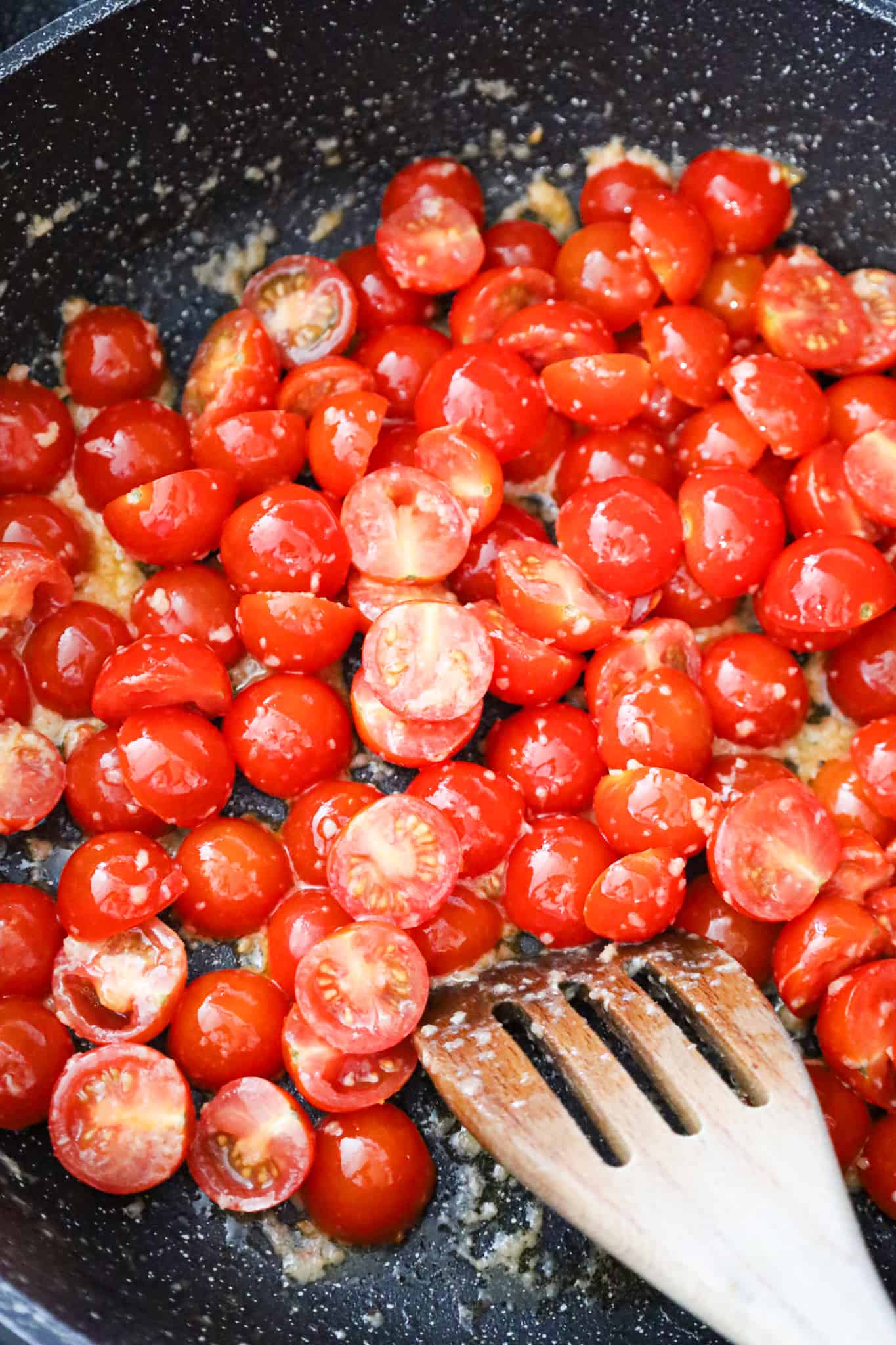 cherry tomatoes tossed in garlic puree and olive oil in a saute pan