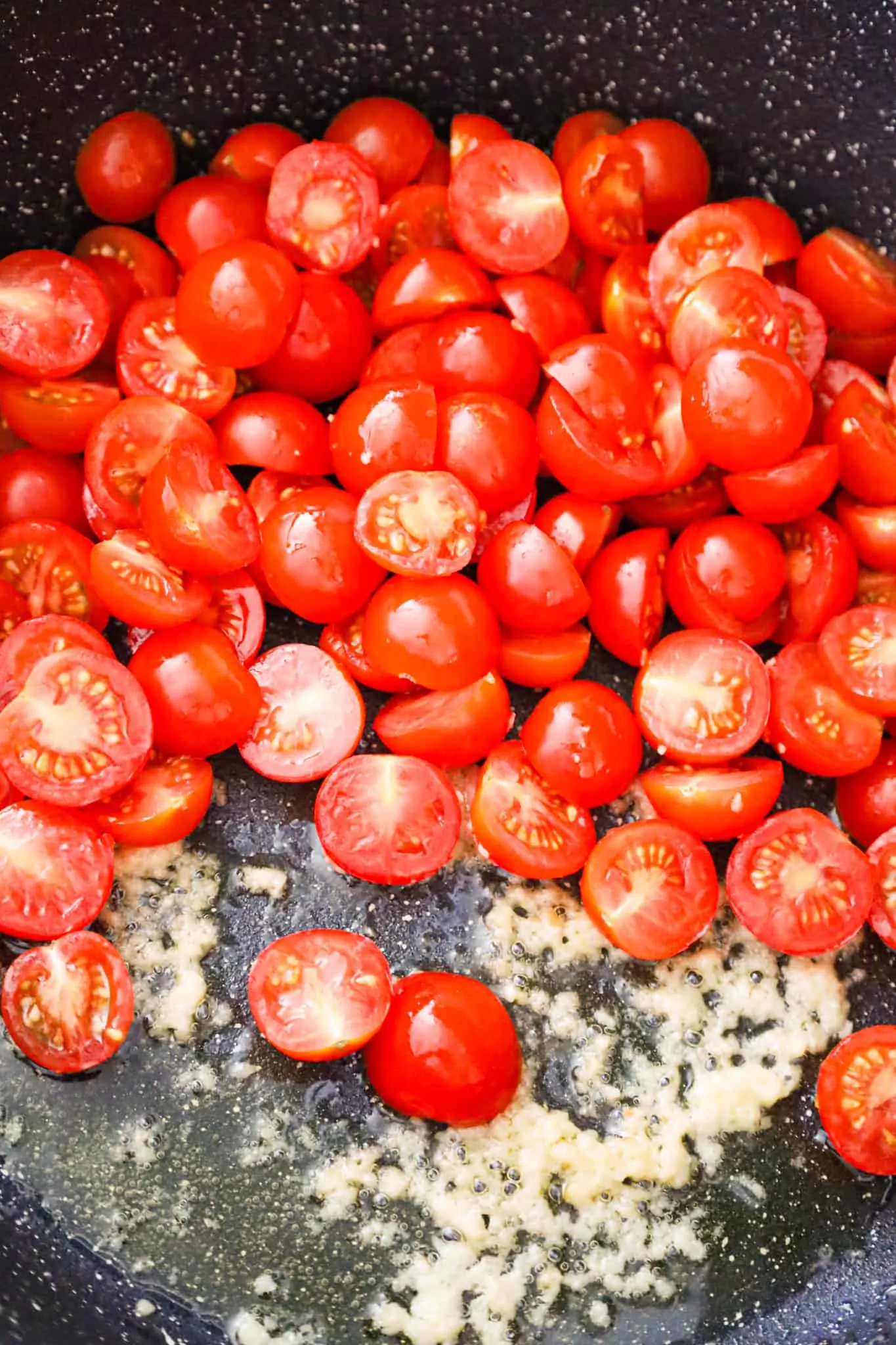 cherry tomato halves on top of garlic puree in a saute pan