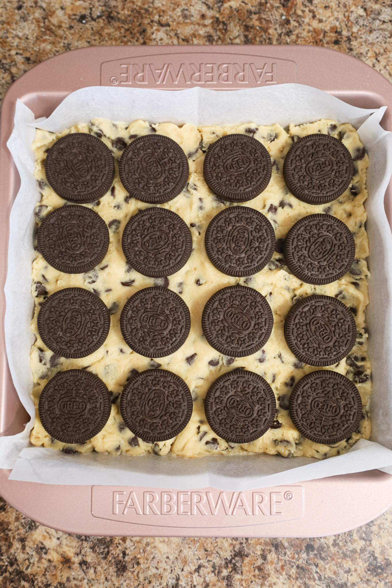 Oreos on top of cookie dough in a parchment lined baking pan