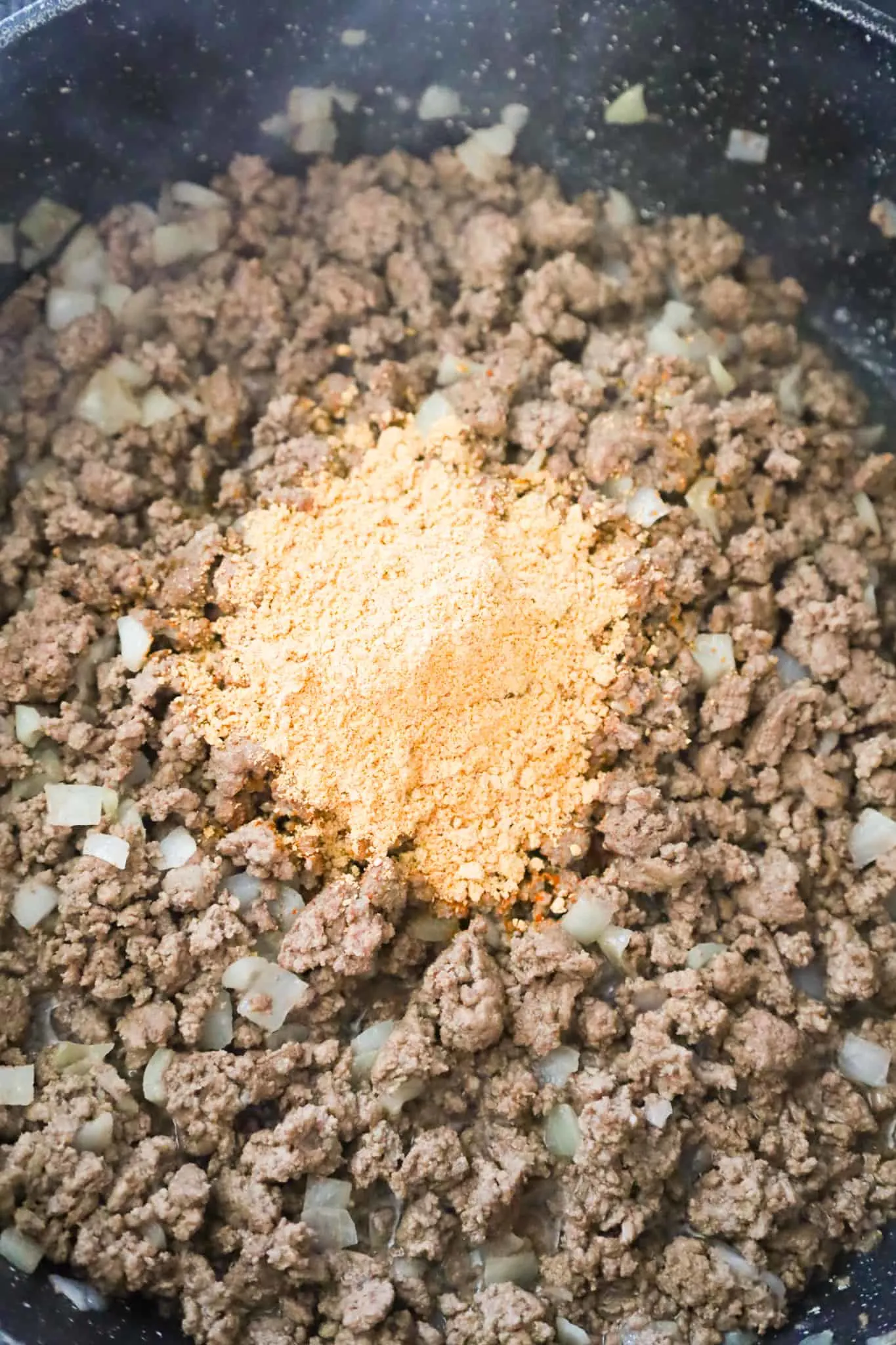 taco seasoning on top of cooked ground beef in a saute pan