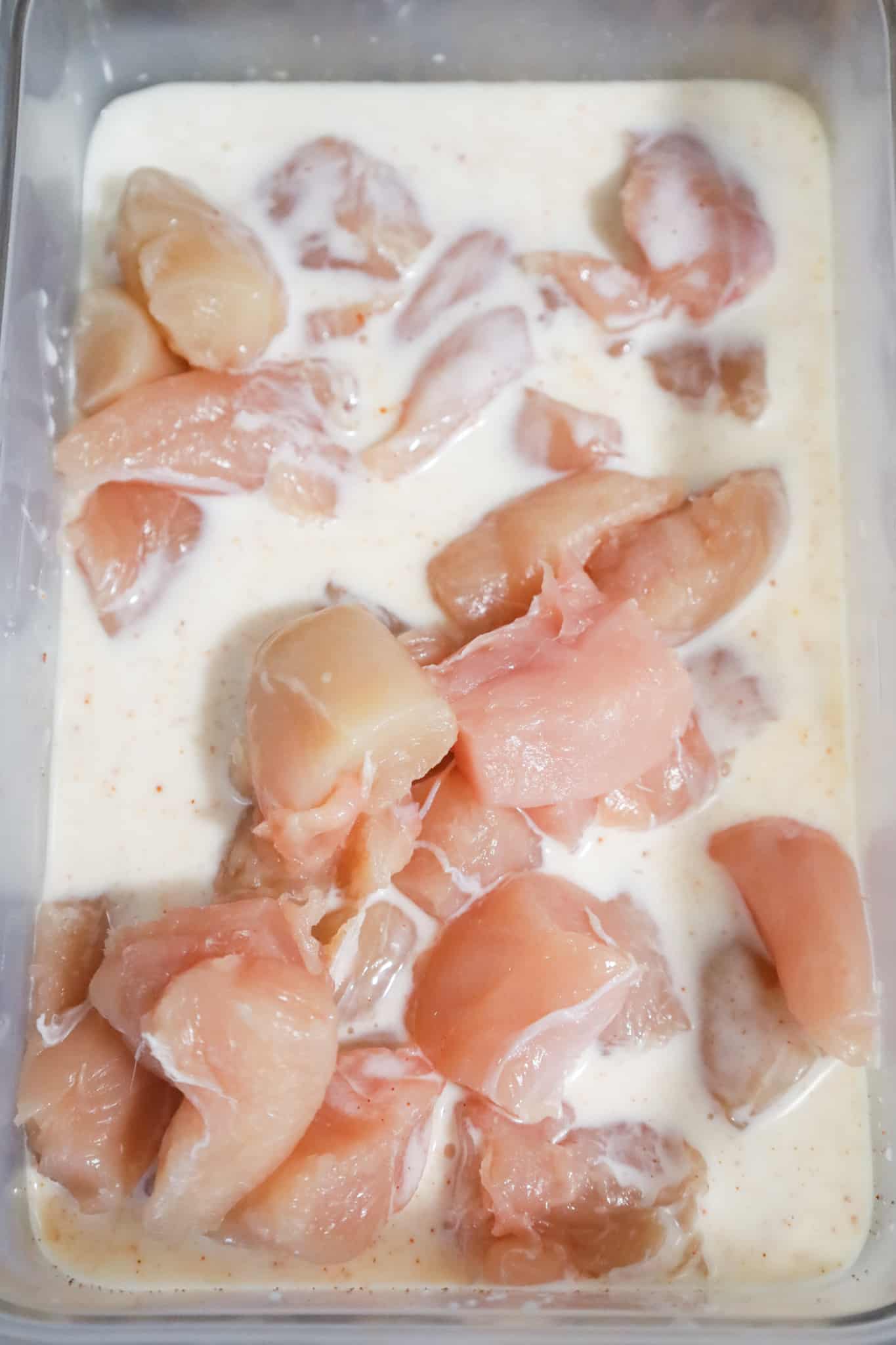 raw chicken breast chunks in buttermilk mixture in a container