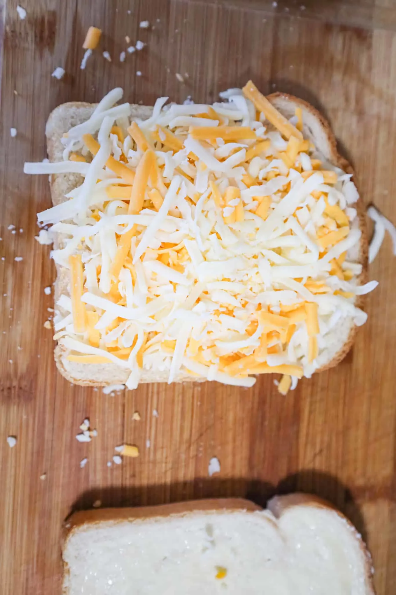 shredded mozzarella and cheddar cheese on top of a slice of bread on a cutting board