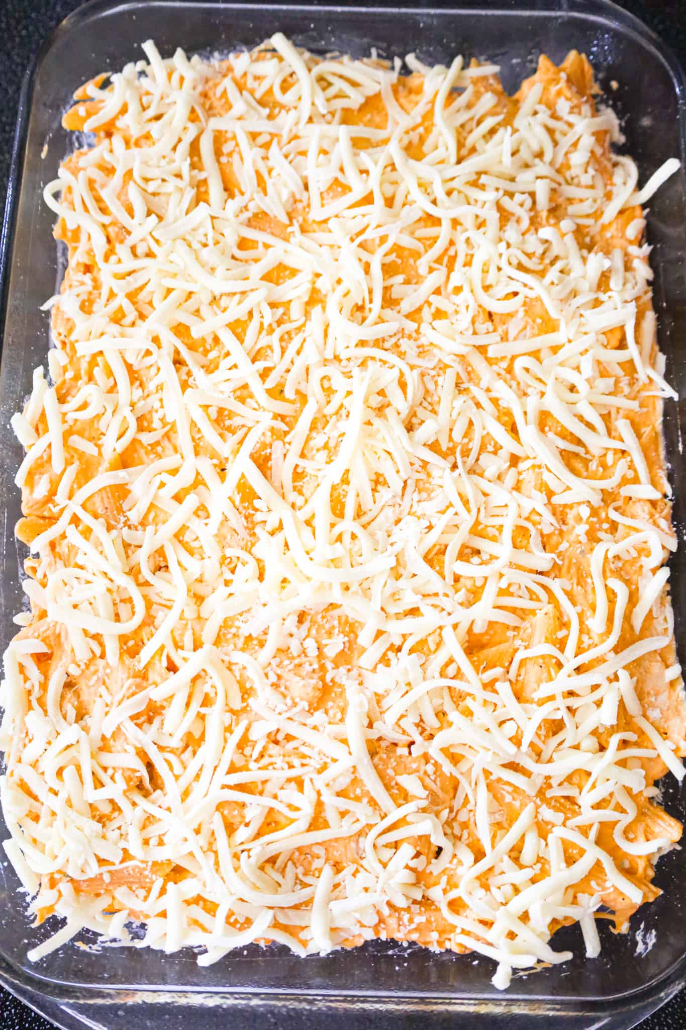 shredded mozzarella cheese on top of buffalo chicken pasta in a baking dish