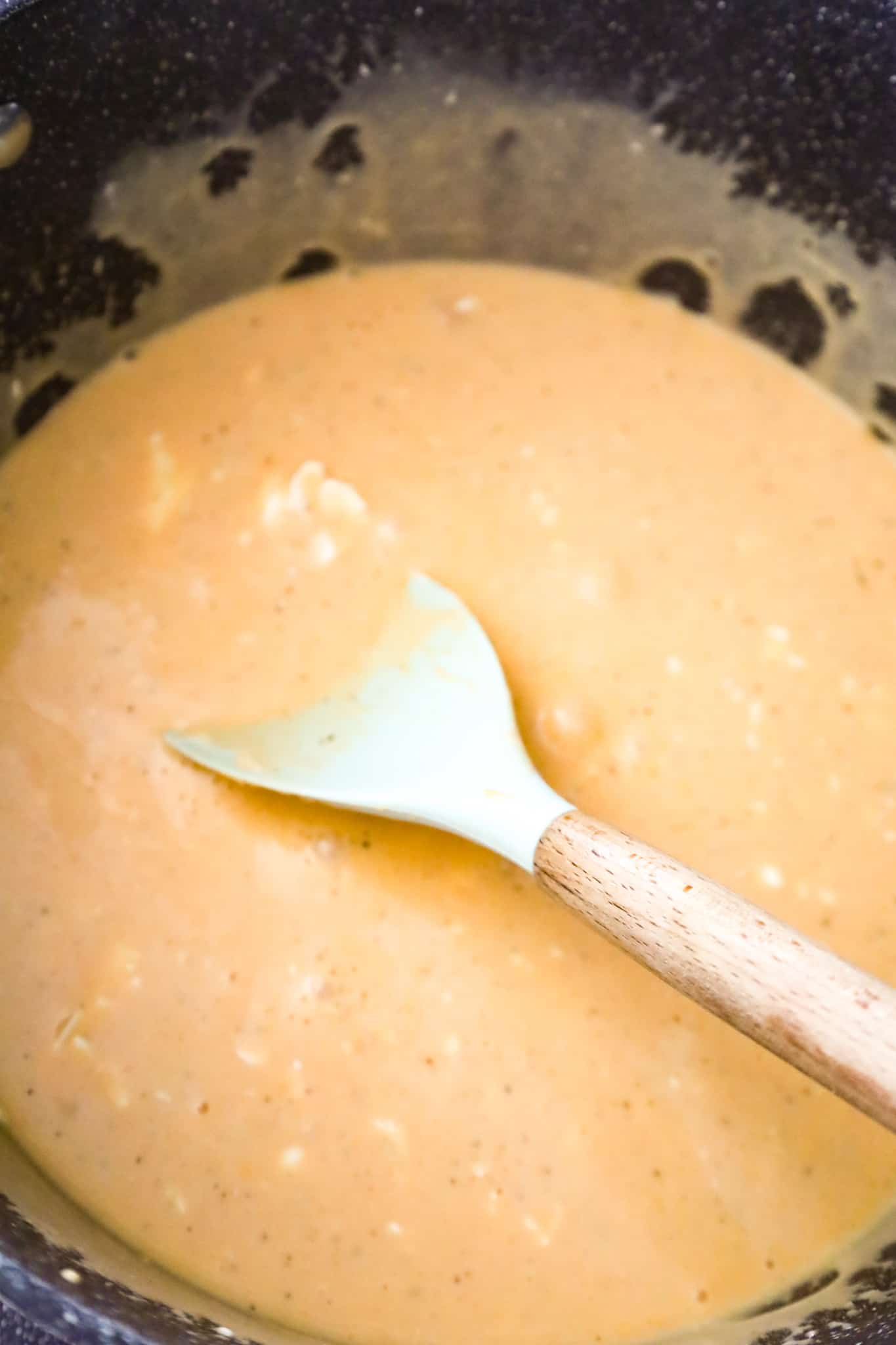 cream cheese being stirred into buffalo sauce in a pot