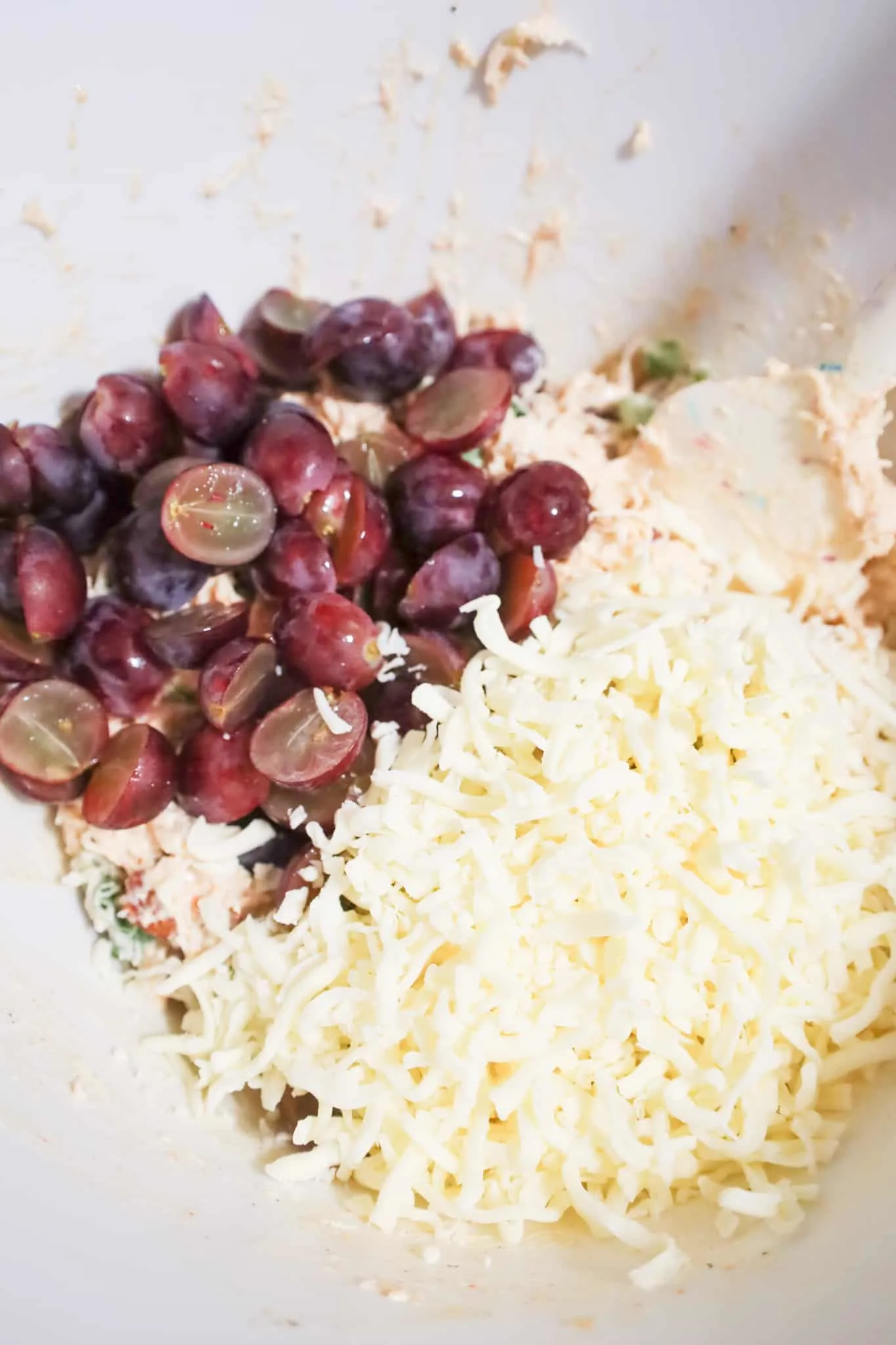 red grape halves and shredded mozzarella cheese on top of shredded chicken in a mixing bowl