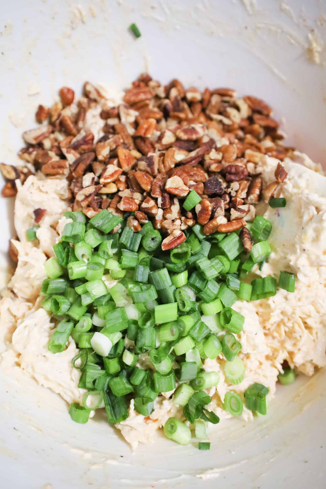 chopped green onions and pecan pieces on top of shredded chicken and mayo mixture in a mixing bowl