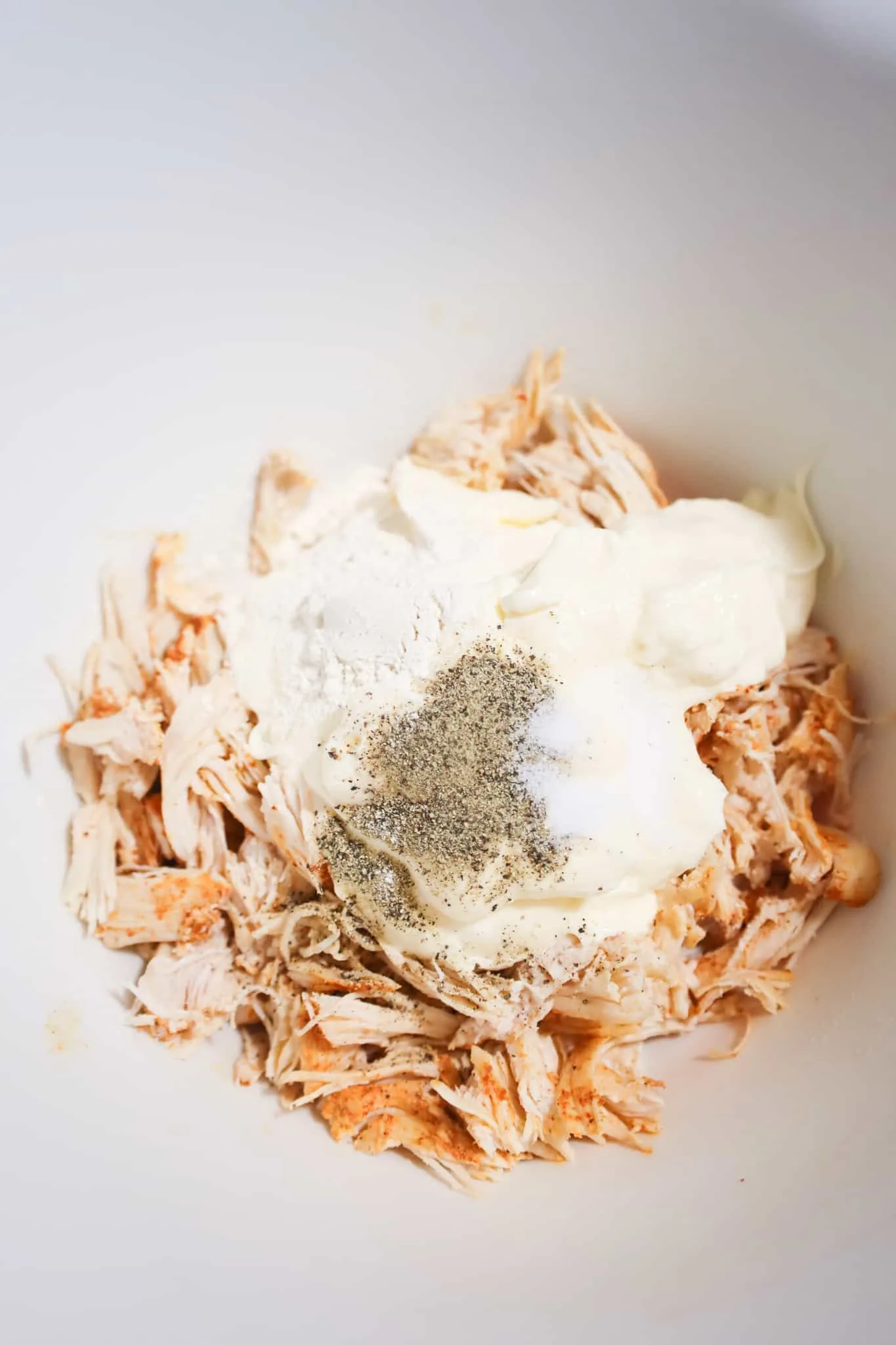 spices and mayo on top of shredded rotisserie chicken in a mixing bowl