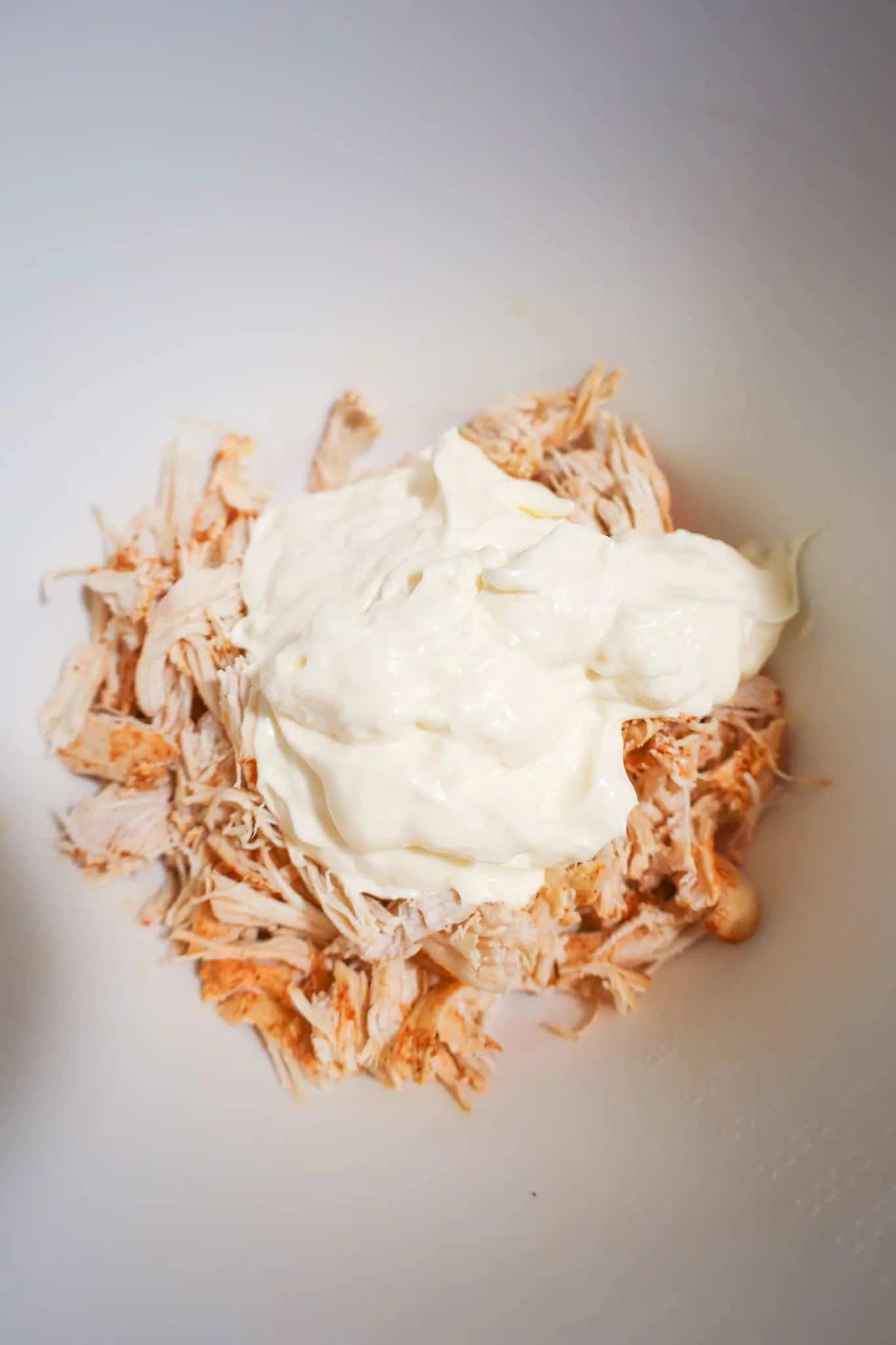 mayo on top of shredded chicken in a mixing bowl