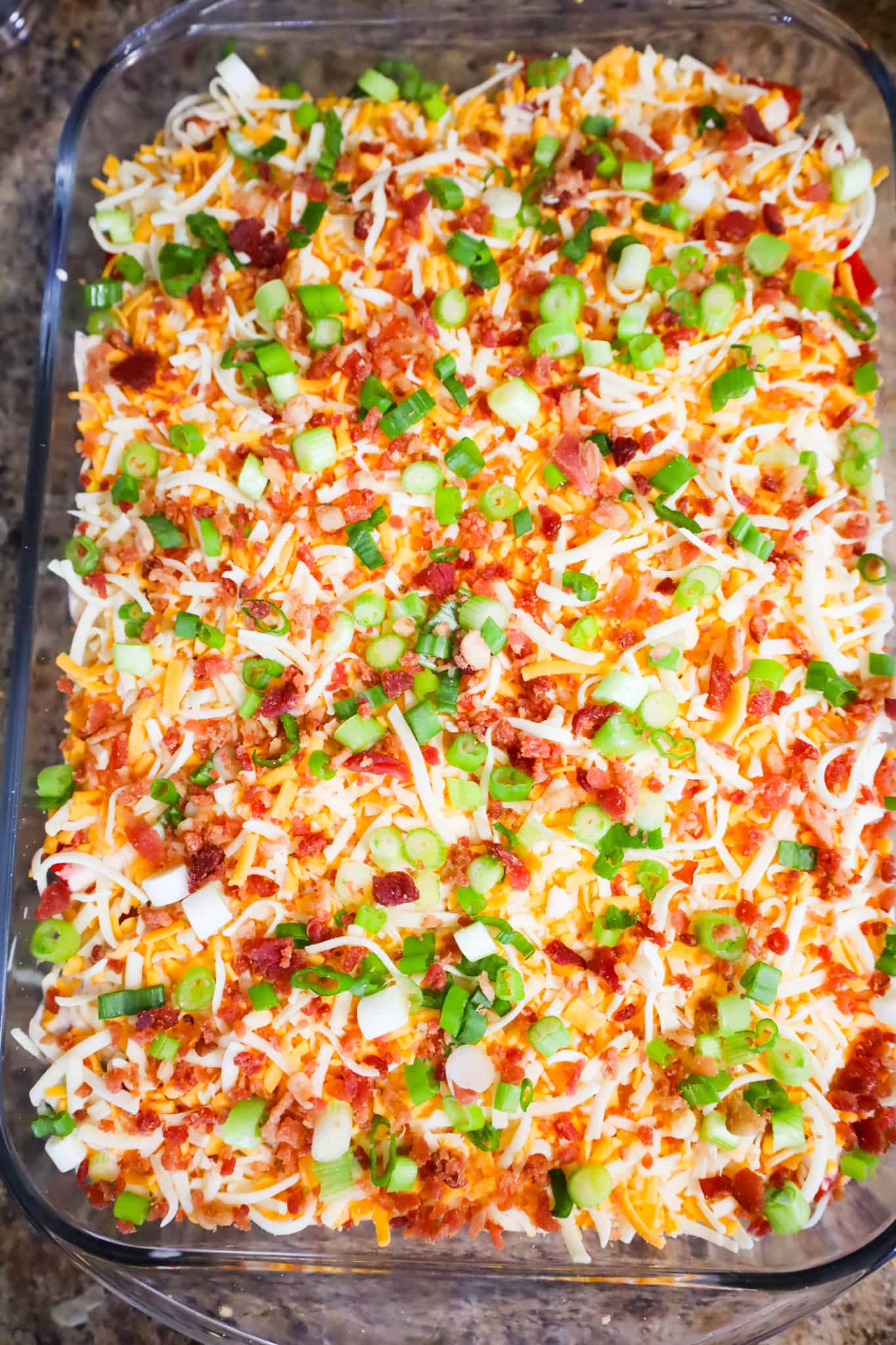chopped green onions, crumbled bacon and shredded cheese on top of cornbread salad in a baking dish