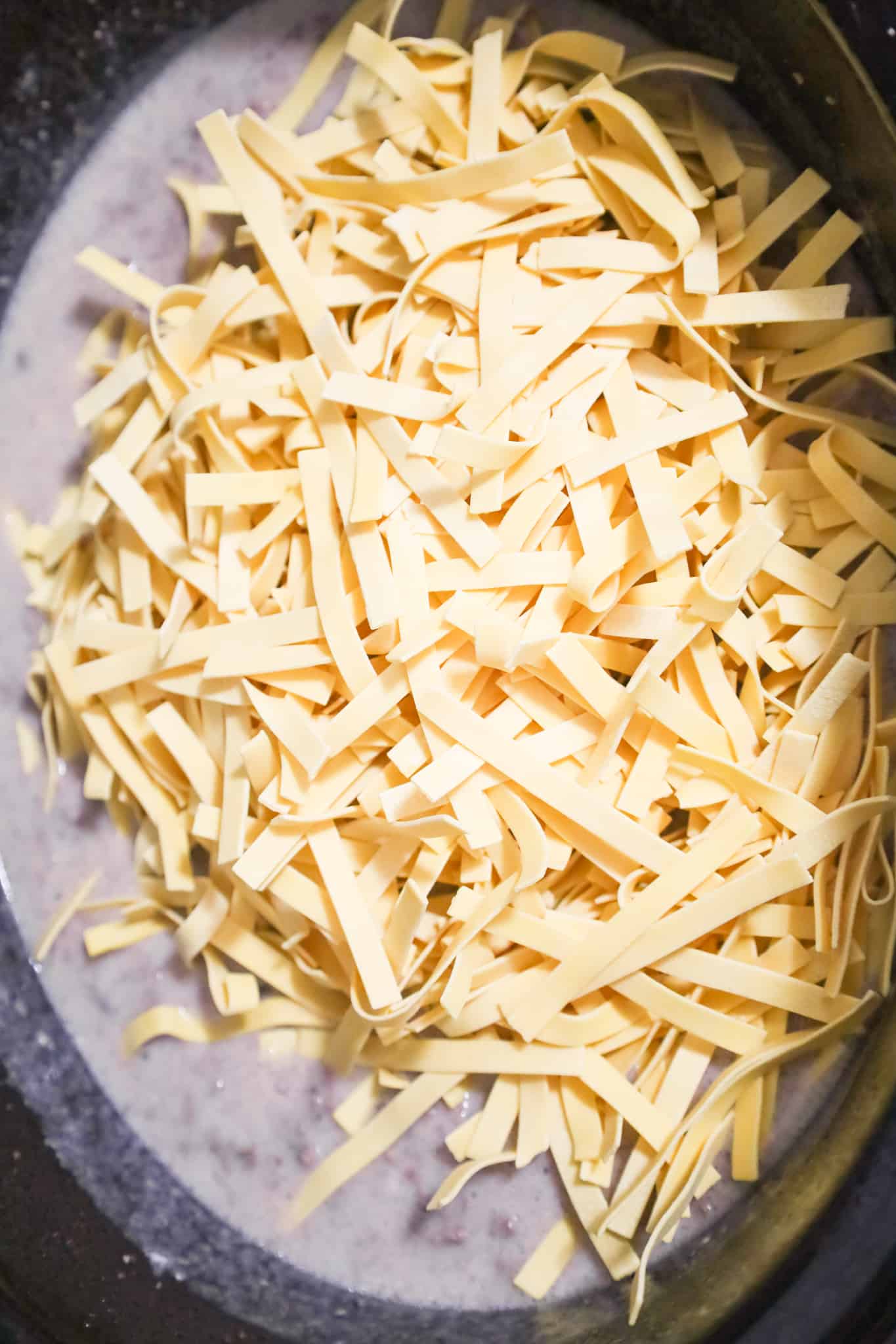 uncooked egg noodles on top of cream of mushroom soup and ground beef mixture in a crock pot