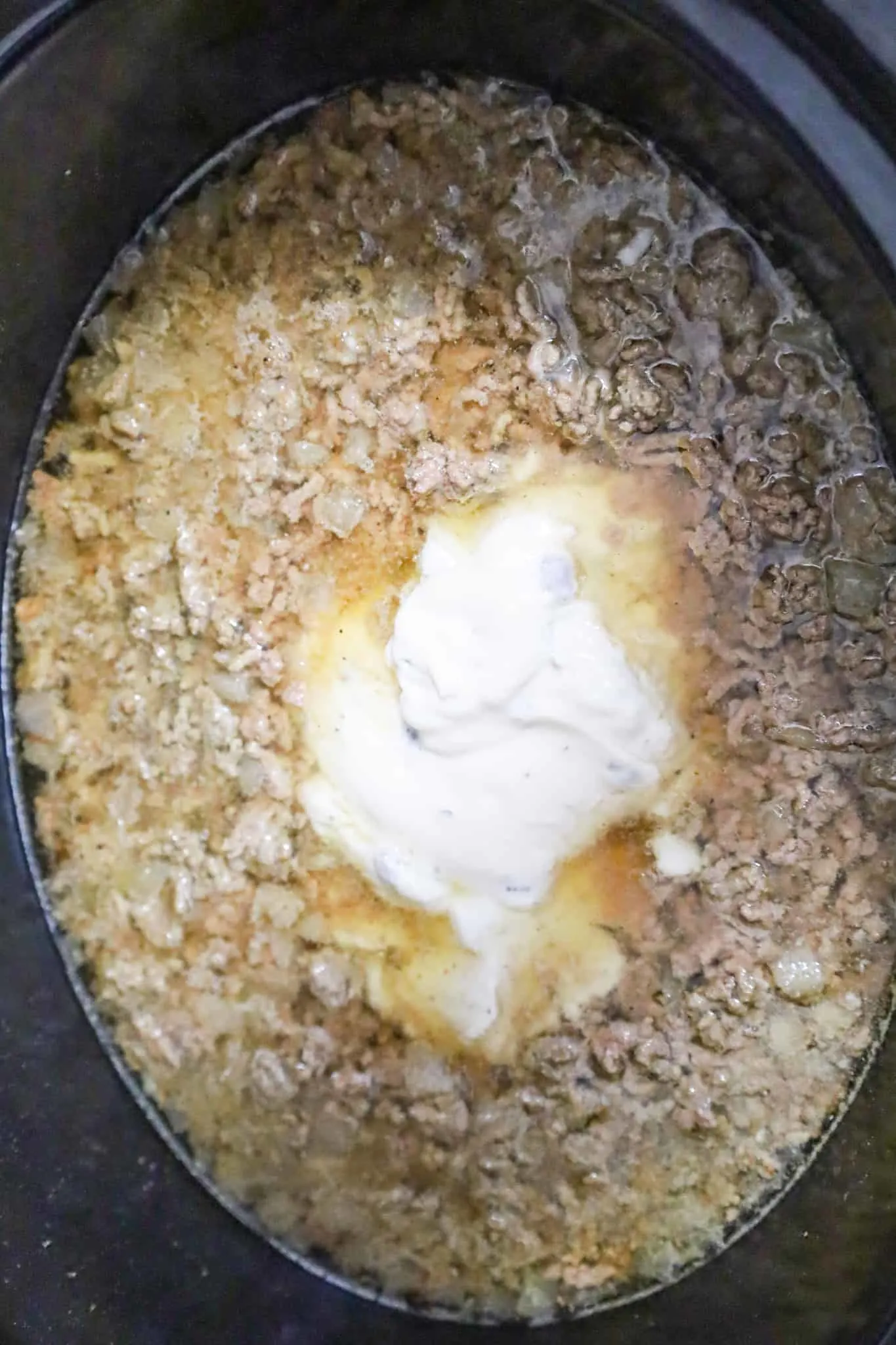 condensed cream of mushroom soup on top of ground beef and beef broth mixture in a crock pot