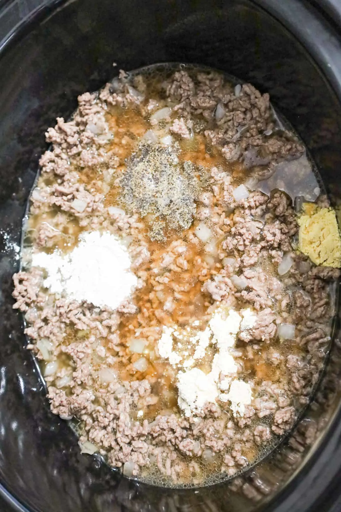 spices on top of ground beef in beef broth in a crock pot