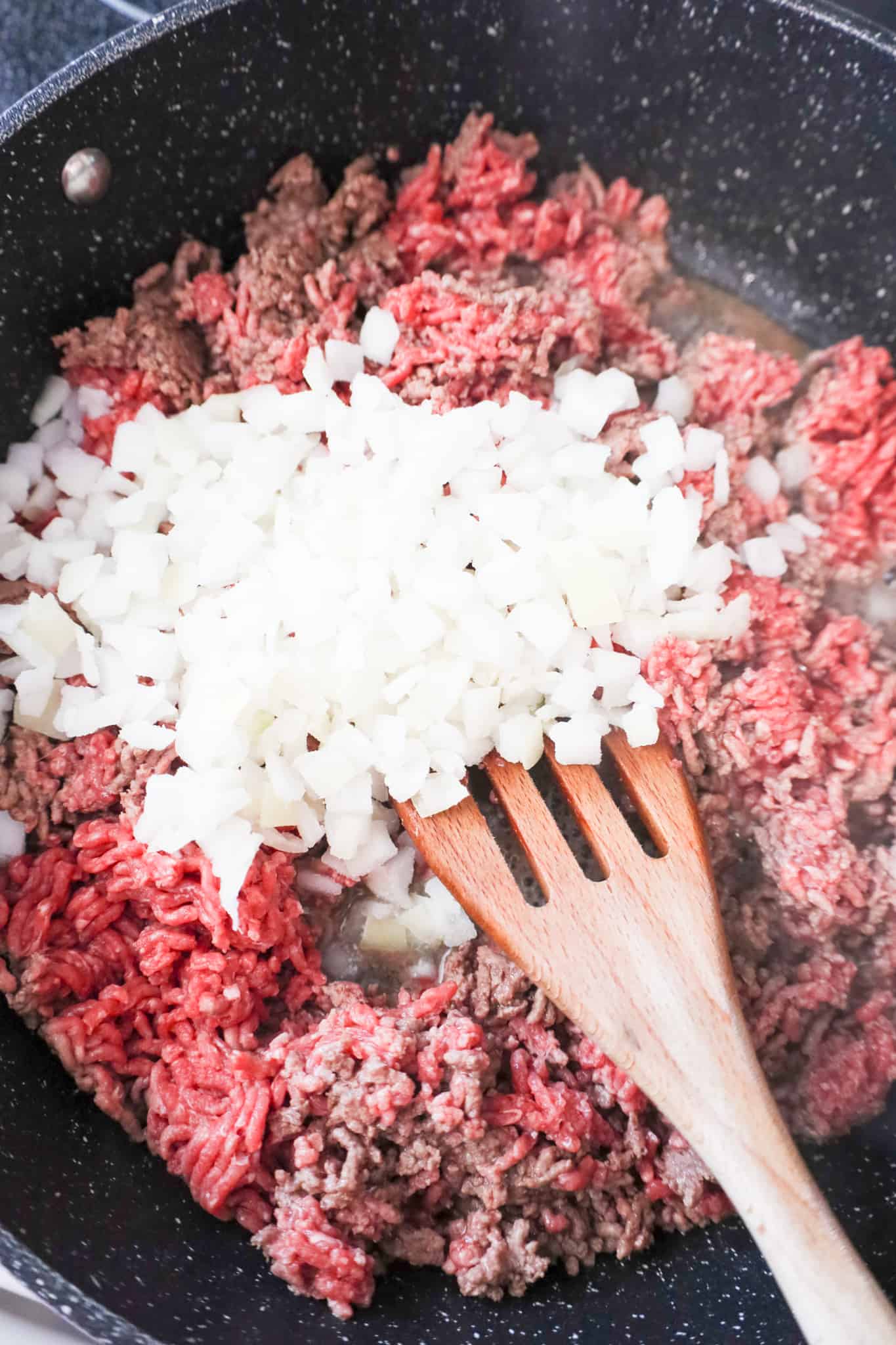 diced onions on top of raw ground beef in a saute pan