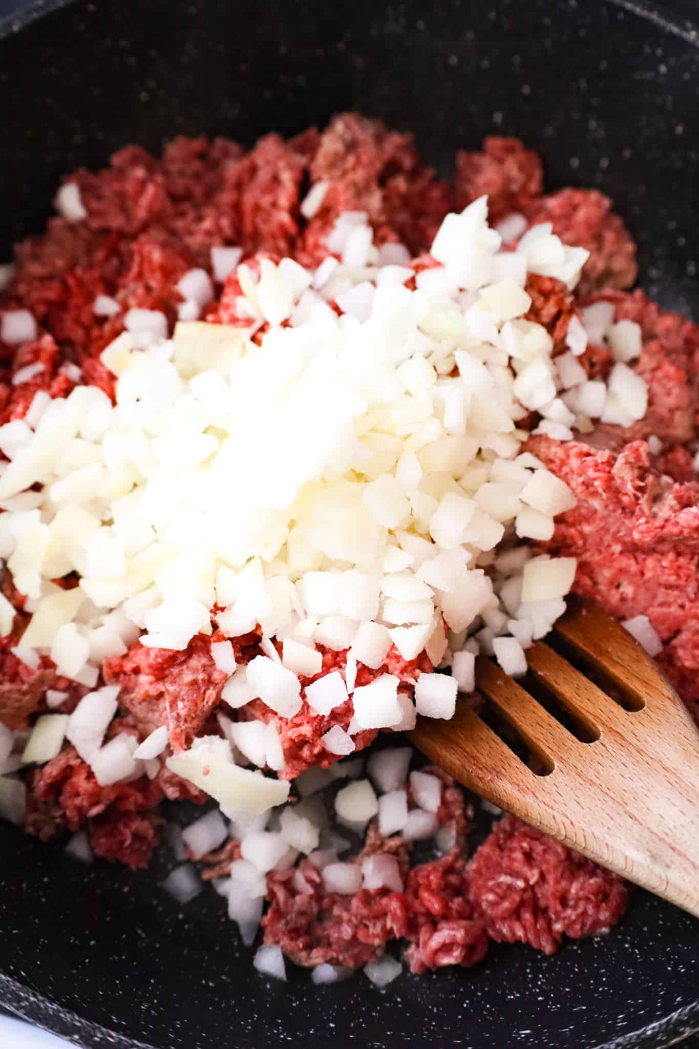 diced onions on top of raw ground beef in a saute pan