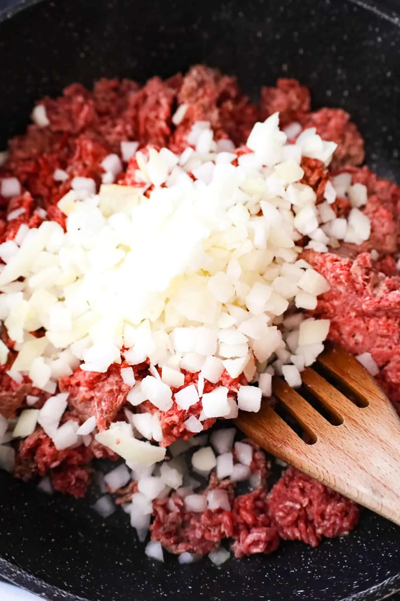 diced onions on top of raw ground beef in a saute pan