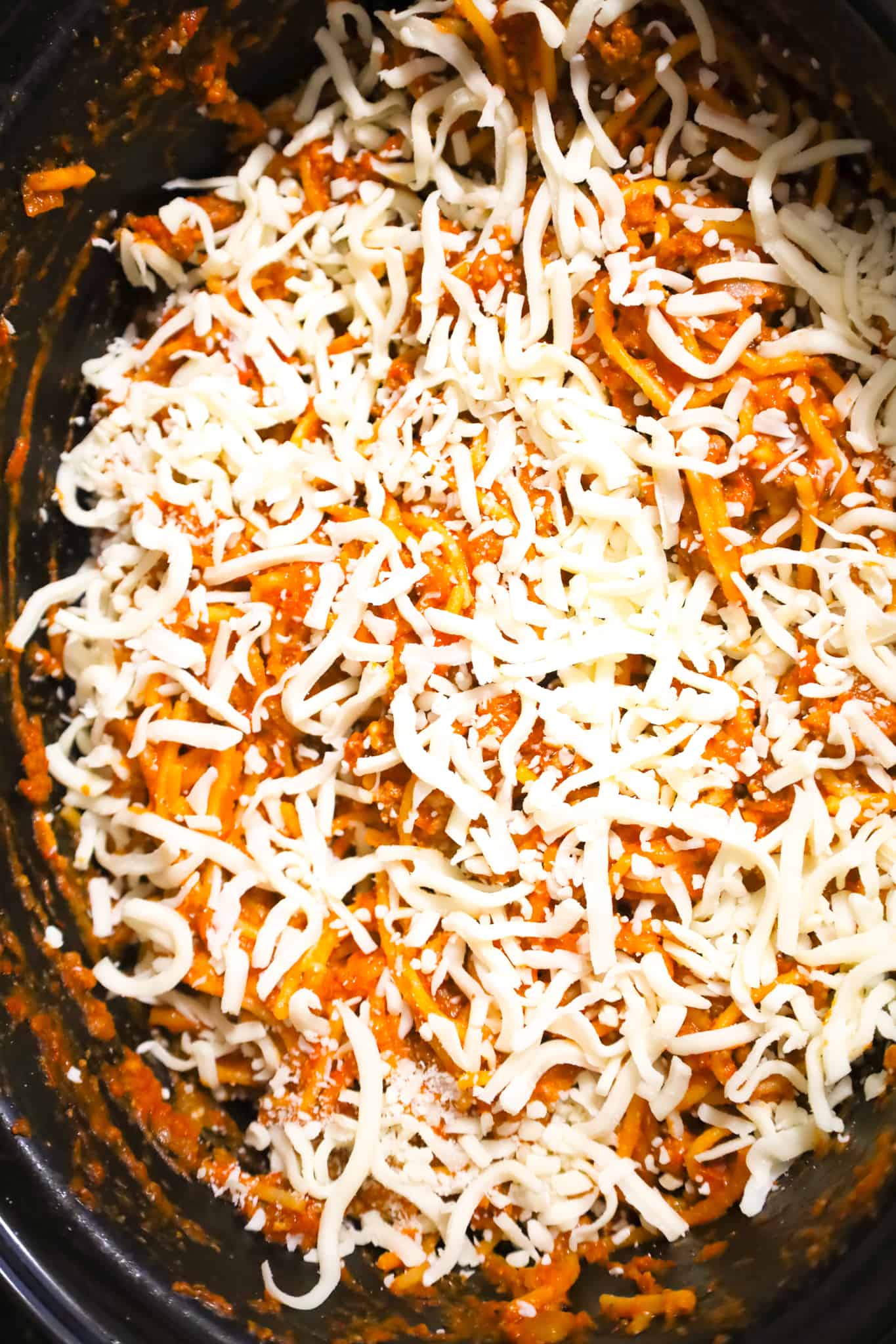shredded mozzarella cheese on top of spaghetti and meat sauce in a crock pot