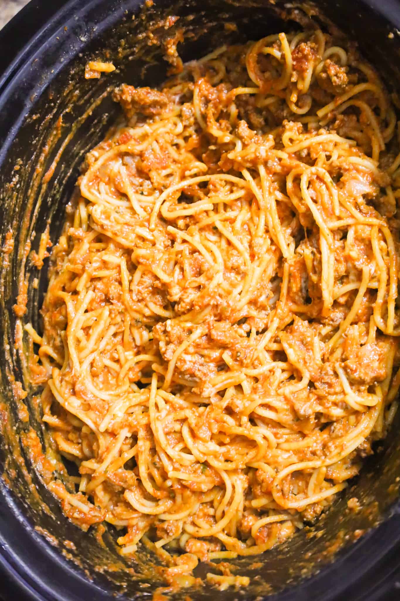 shredded mozzarella cheese on top of spaghetti and meat sauce in a crock pot