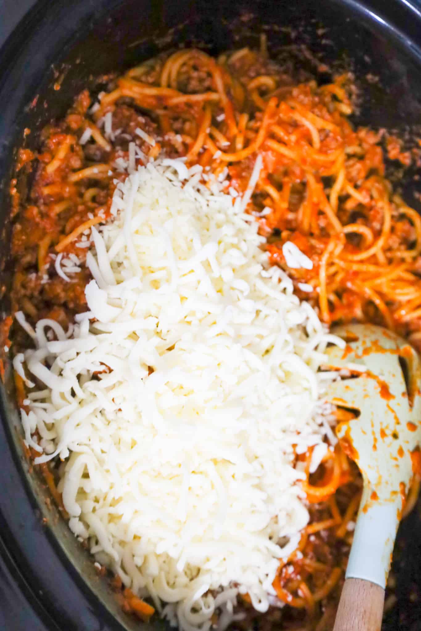 shredded mozzarella and parmesan cheese on top of spaghetti and meat sauce in a crock pot