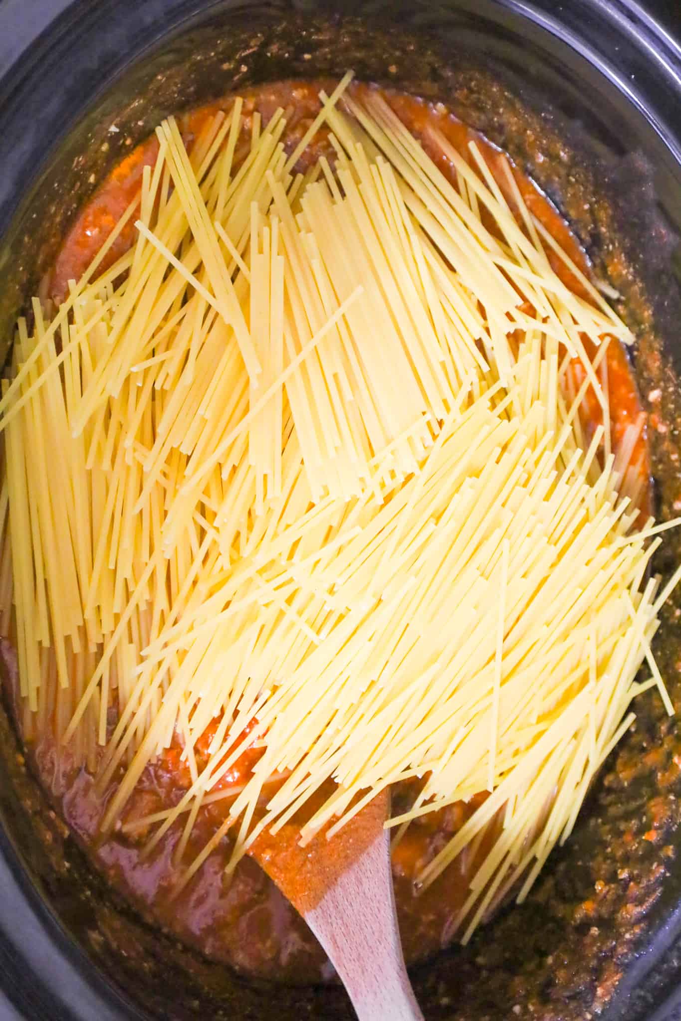 uncooked spaghetti noodles mixed into meat sauce in a crock pot