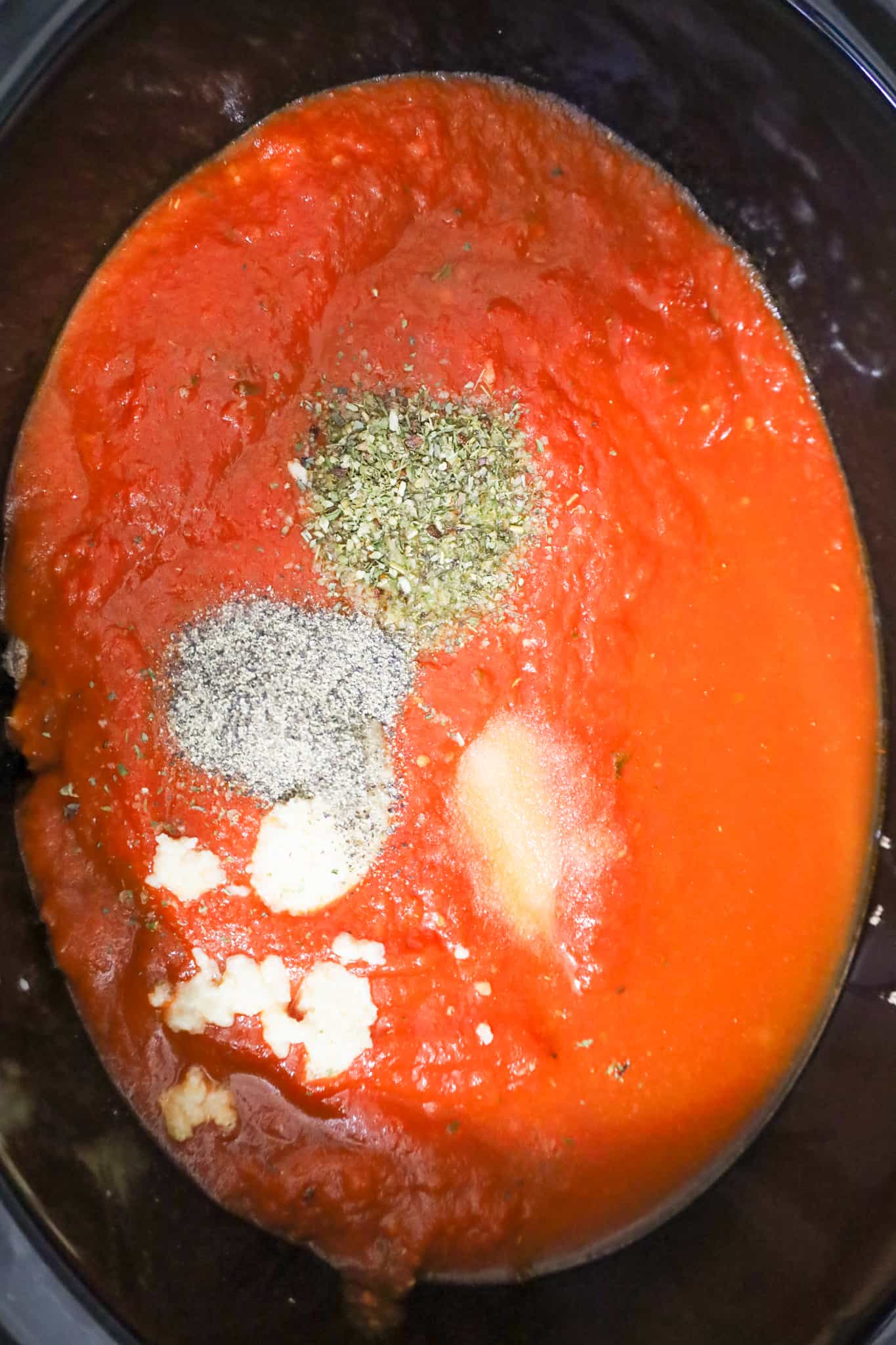 spices on top of marinara sauce in a crock pot