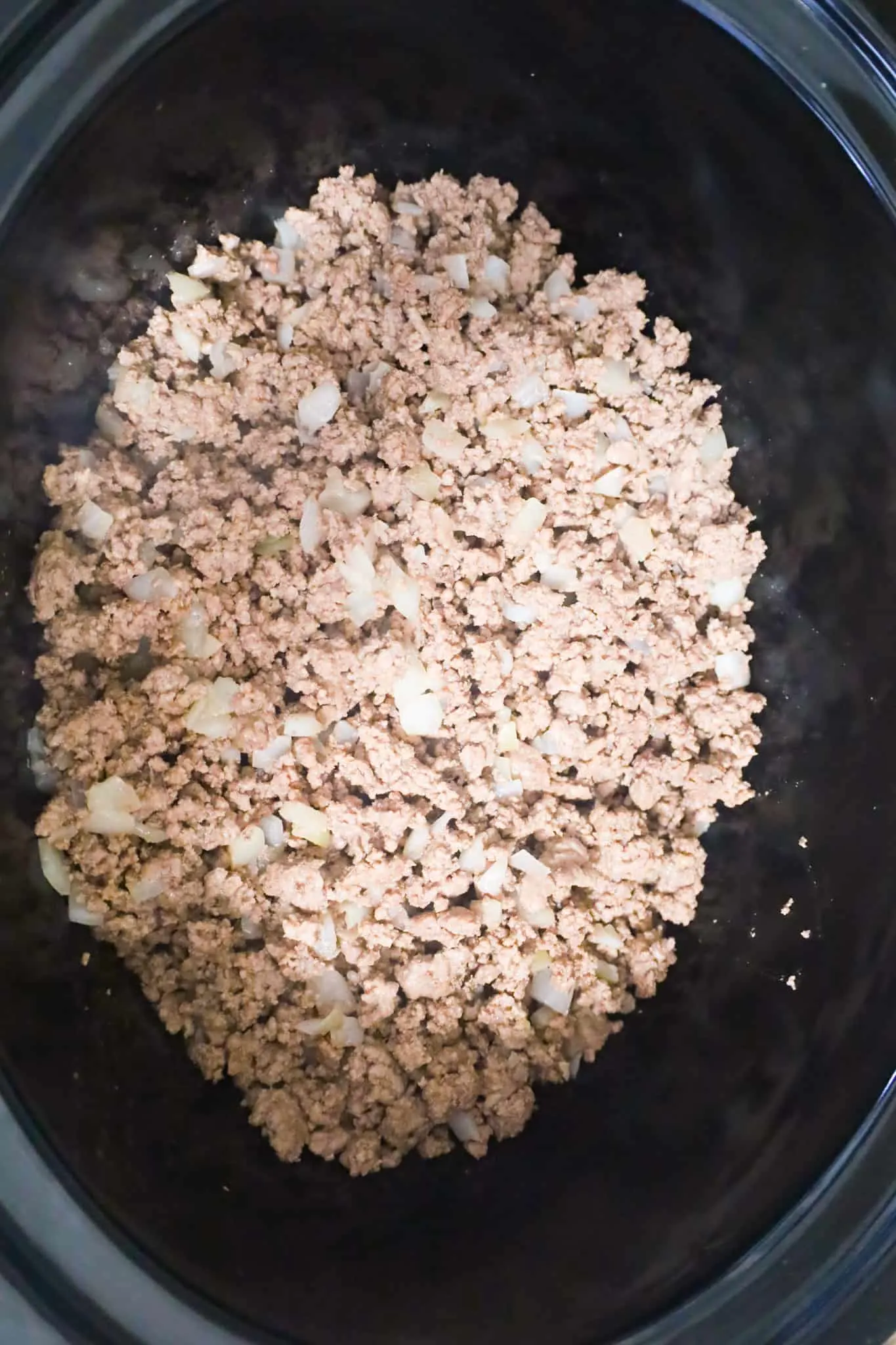 cooked ground beef and diced onions in the bottom of a crock pot