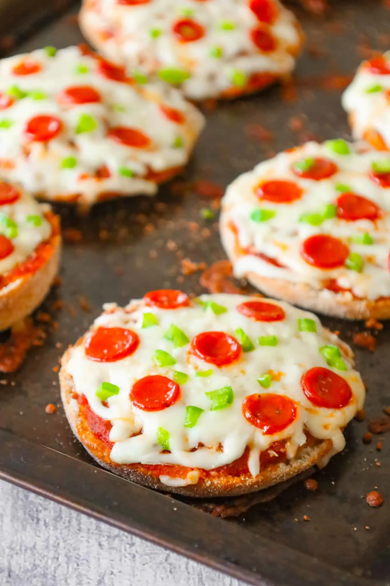 English Muffin Pizzas are an easy dinner recipe made with split English muffins topped with pizza sauce, shredded mozzarella cheese, mini pepperonis and diced green peppers.