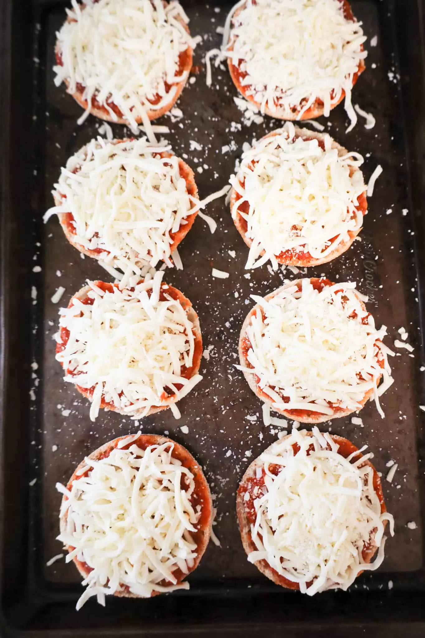 shredded mozzarella cheese on top of pizza sauce on English muffins