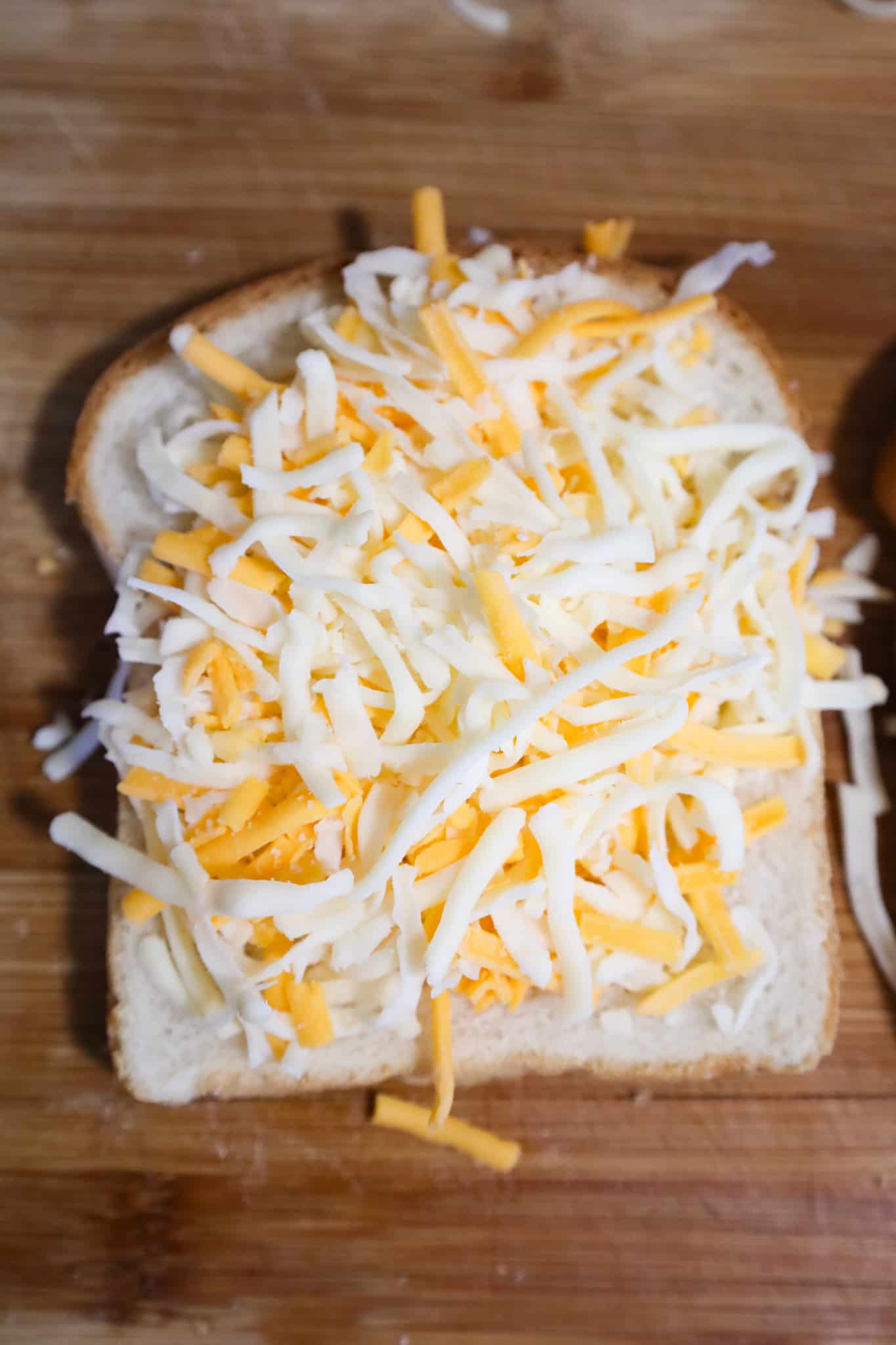 shredded mozzarella and cheddar cheese on top of a slice of bread on a cutting board