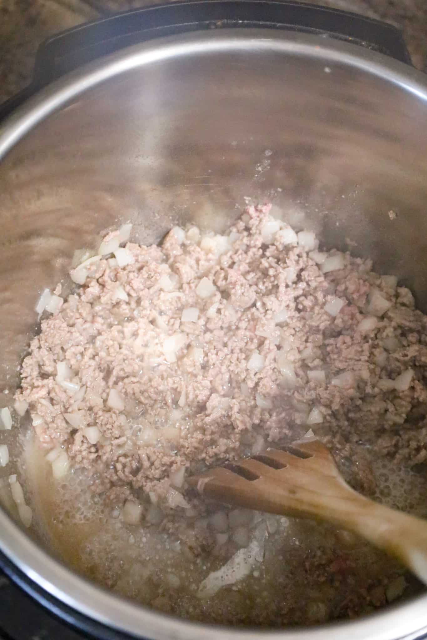 ground beef and diced onions cooking in a pressure cooker