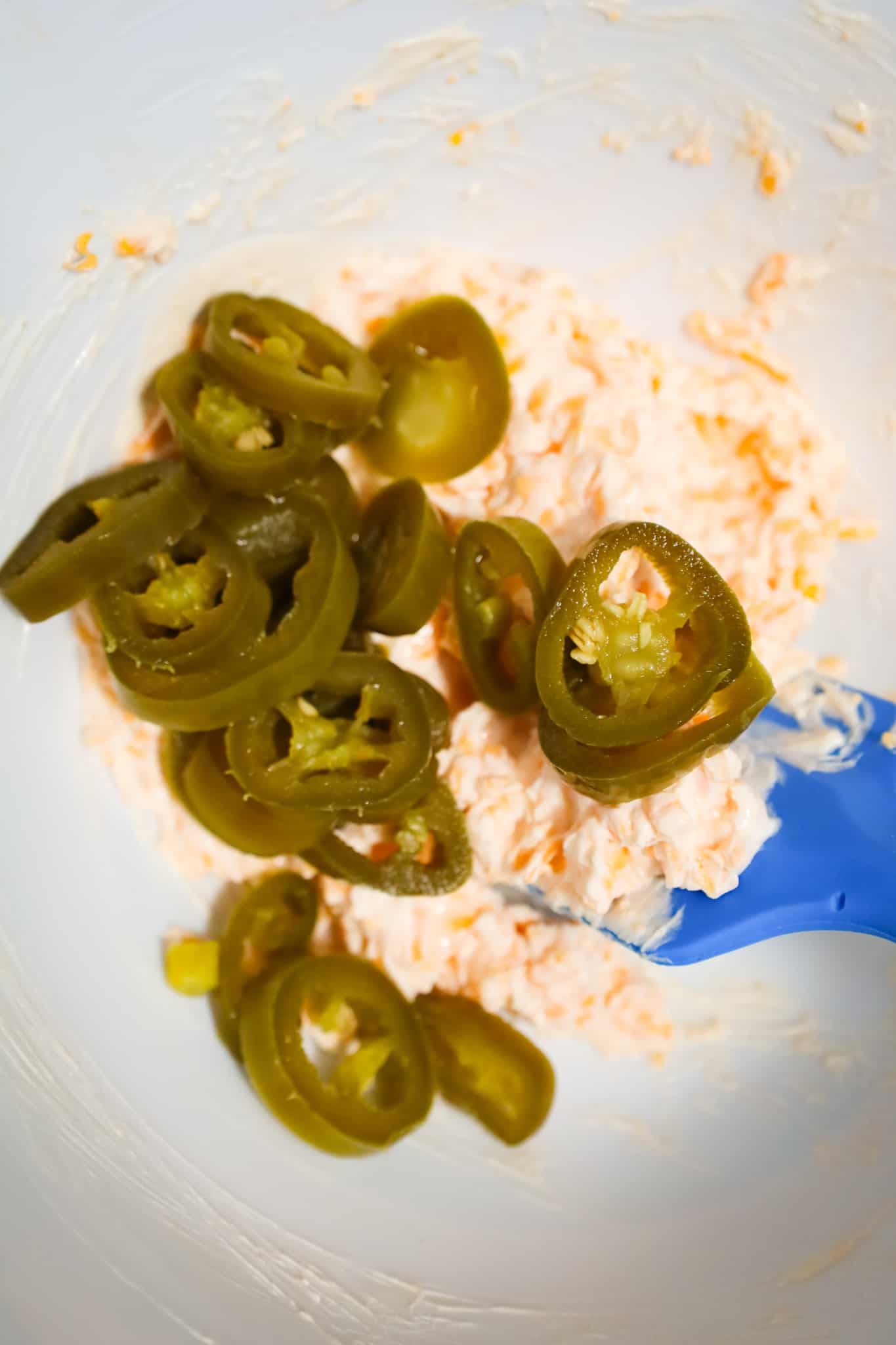 sliced jalapenos on top of cheese mixture in a mixing bowl