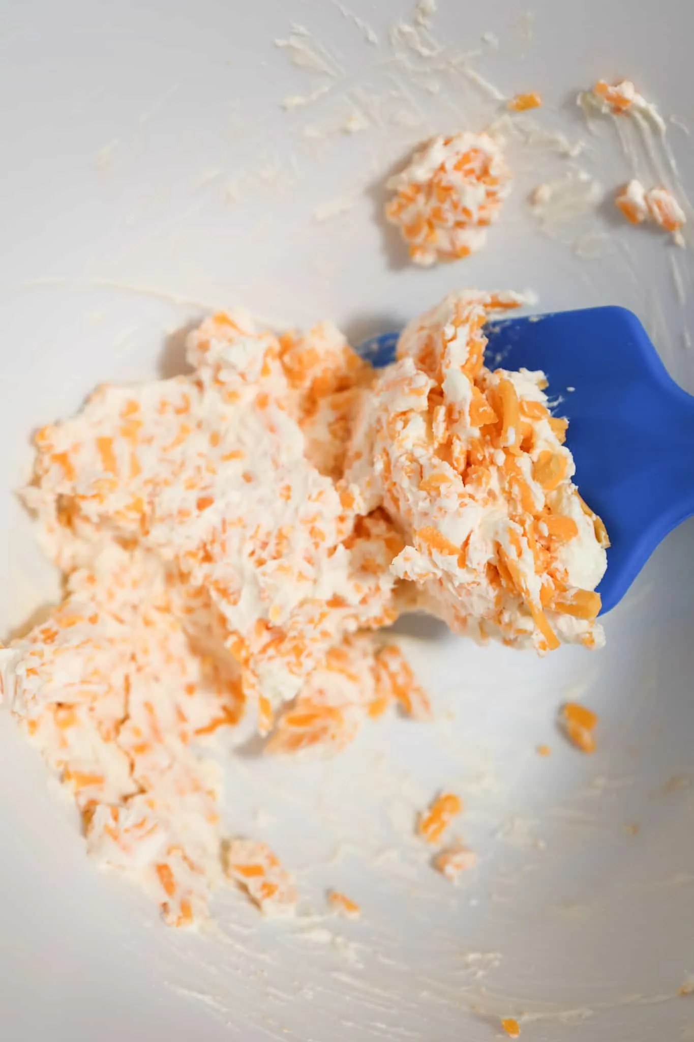 cream cheese and shredded cheese being stirred together in a mixing bowl