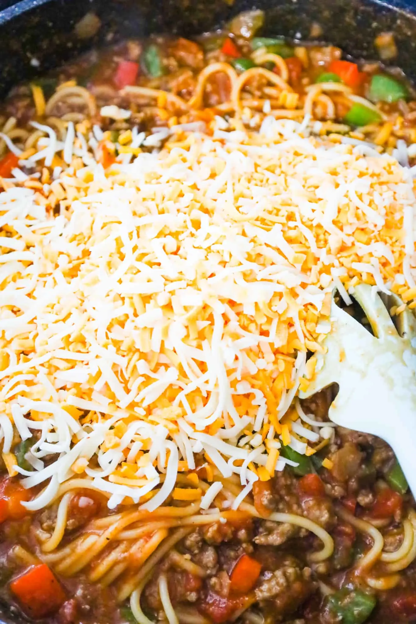 shredded cheese on top of Mexican spaghetti in a saute pan