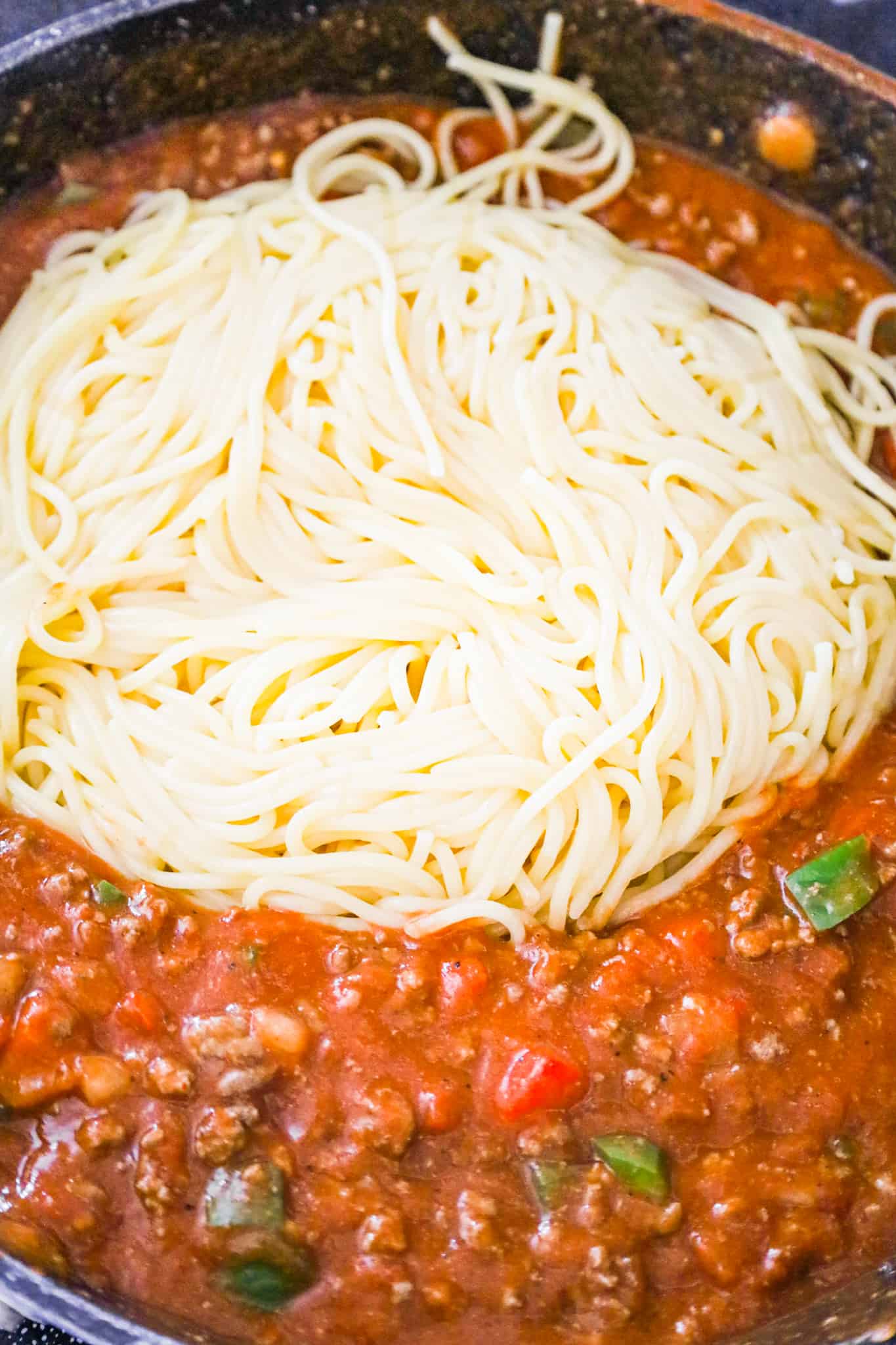 cooked spaghetti added to tomato sauce and ground beef mixture in a saute pan