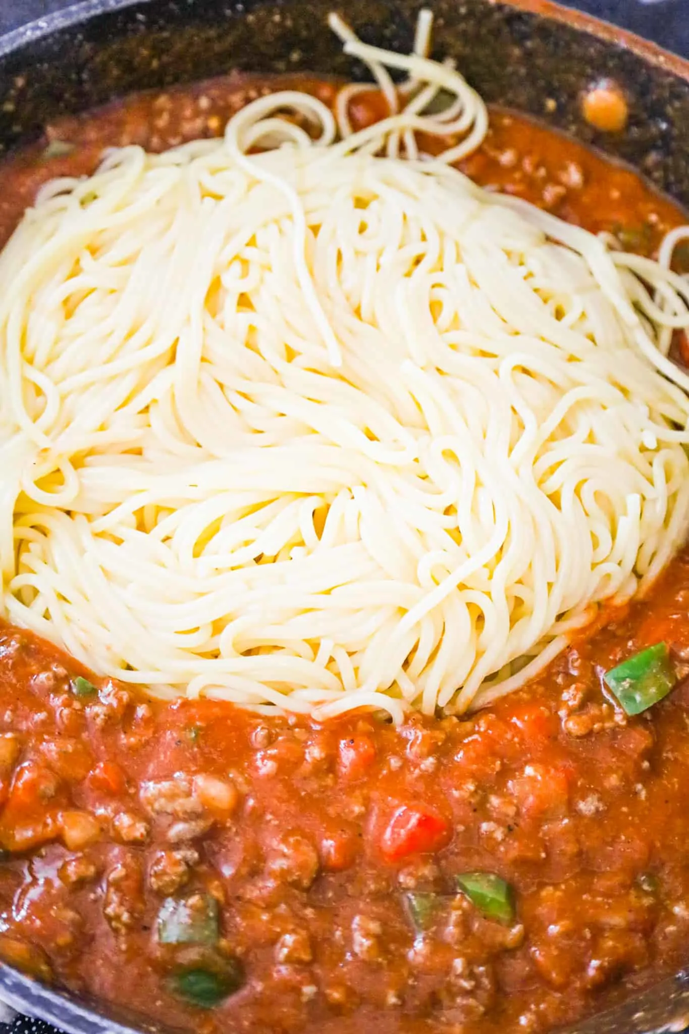 cooked spaghetti added to tomato sauce and ground beef mixture in a saute pan