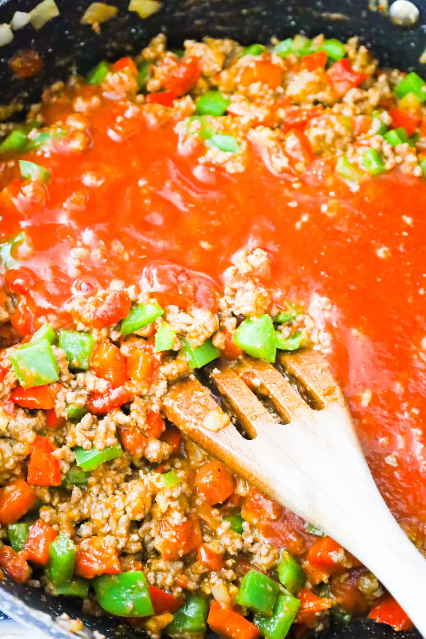 tomato sauce added to ground beef and peppers mixture in a saute pan