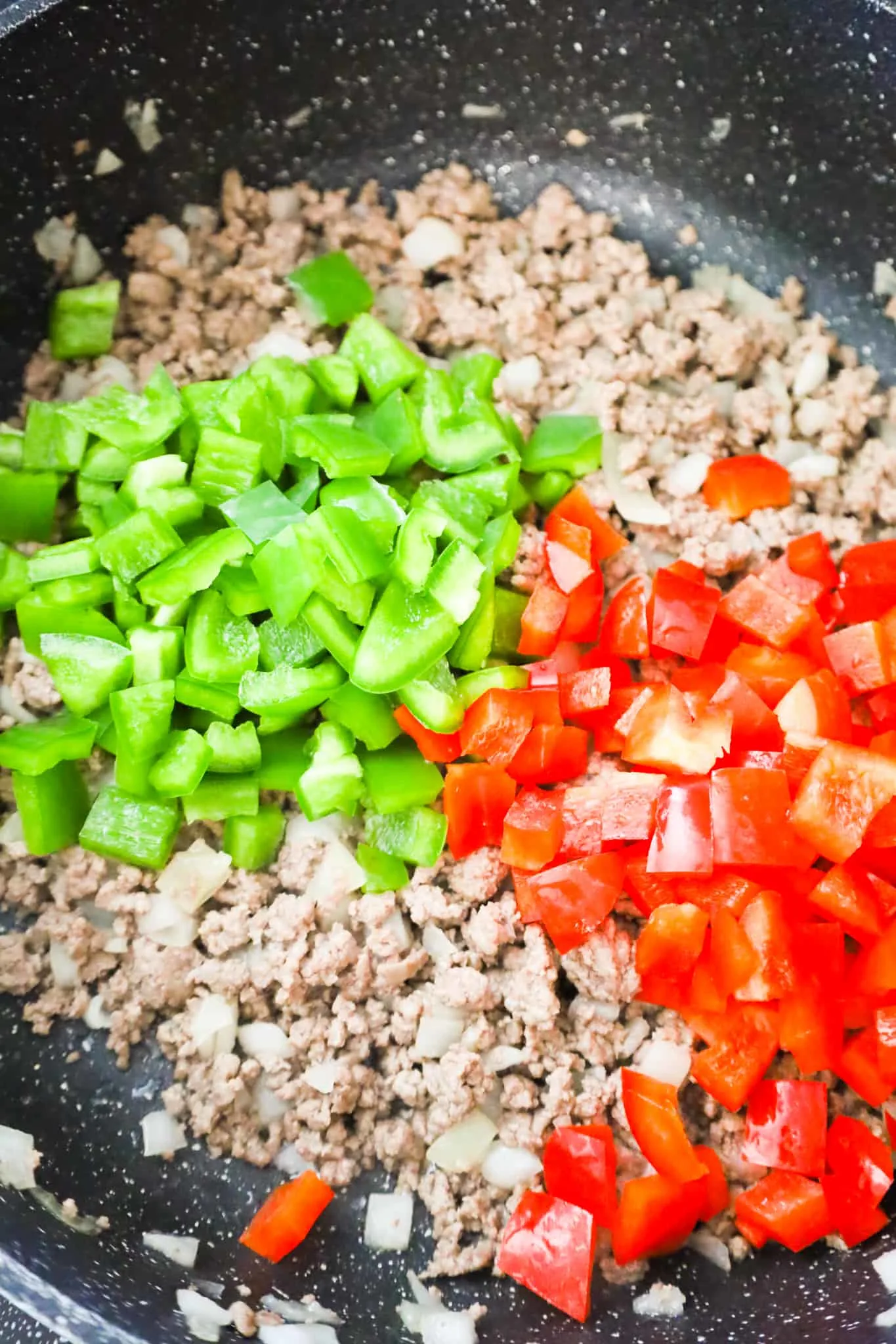 diced red and green peppers on top of cooked ground beef in a saute pan