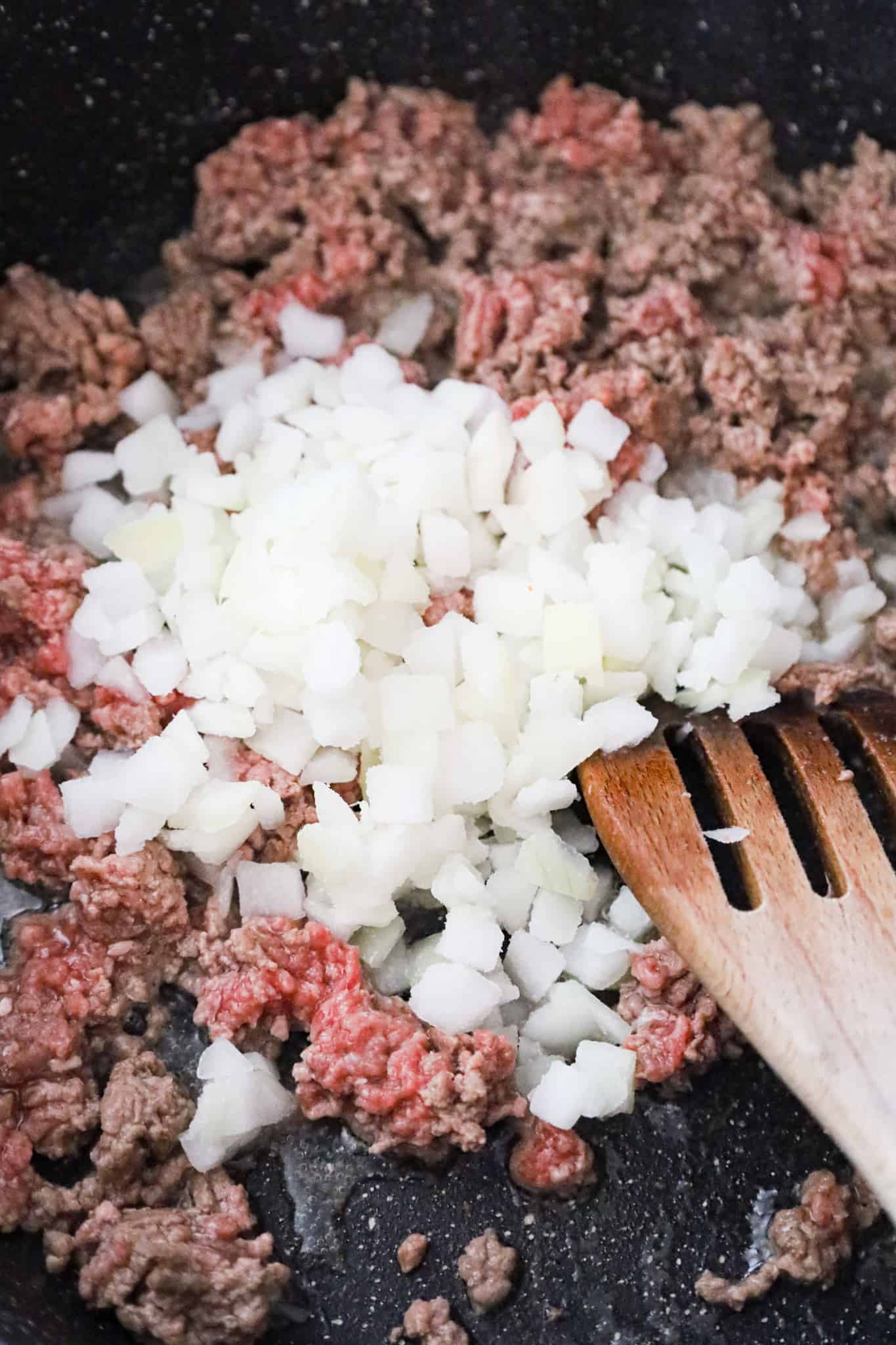 diced onions on top of raw ground beef in a saute pan