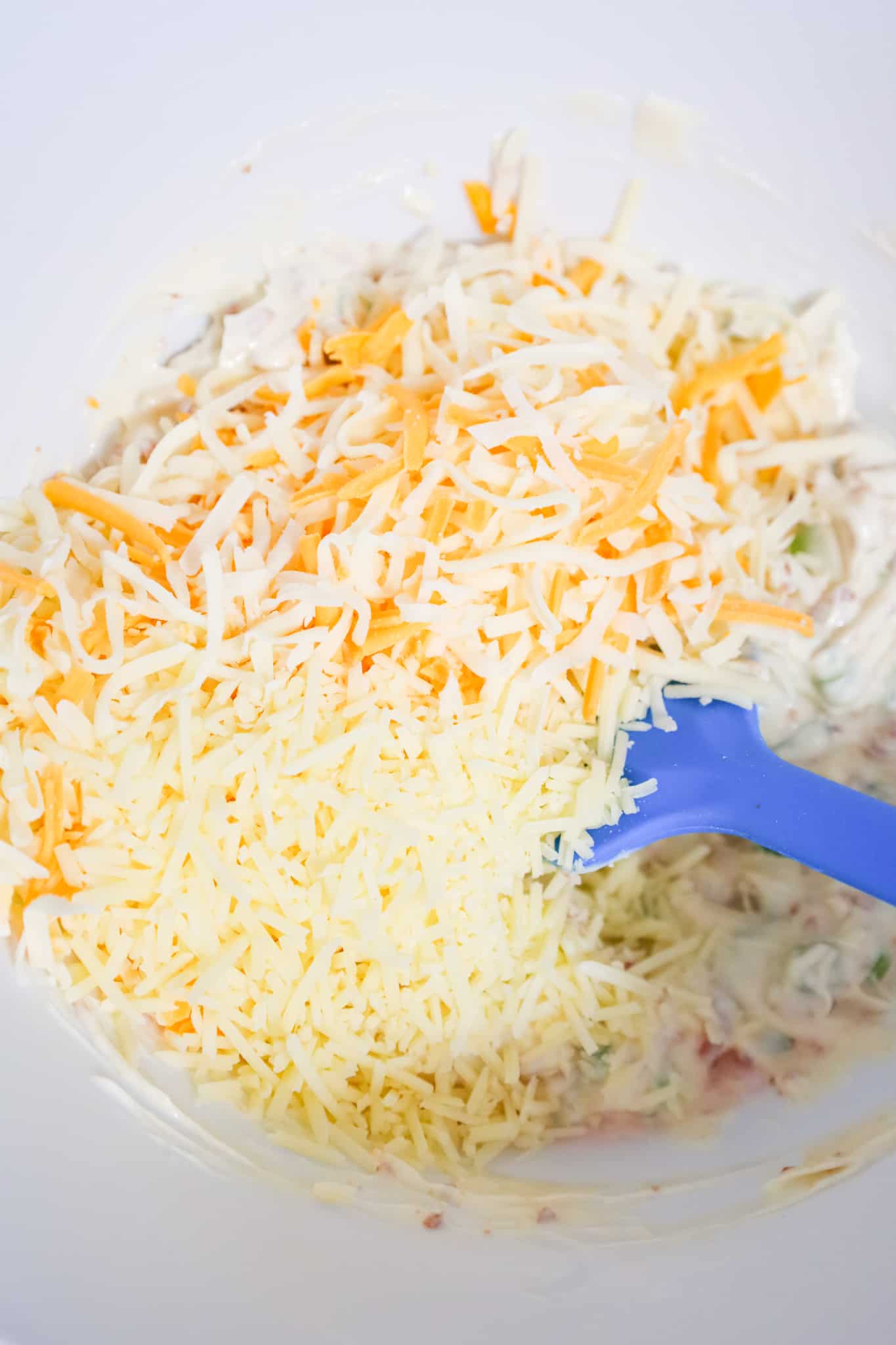 shredded parmesan, mozzarella and cheddar cheese on top of mayo mixture in a mixing bowl