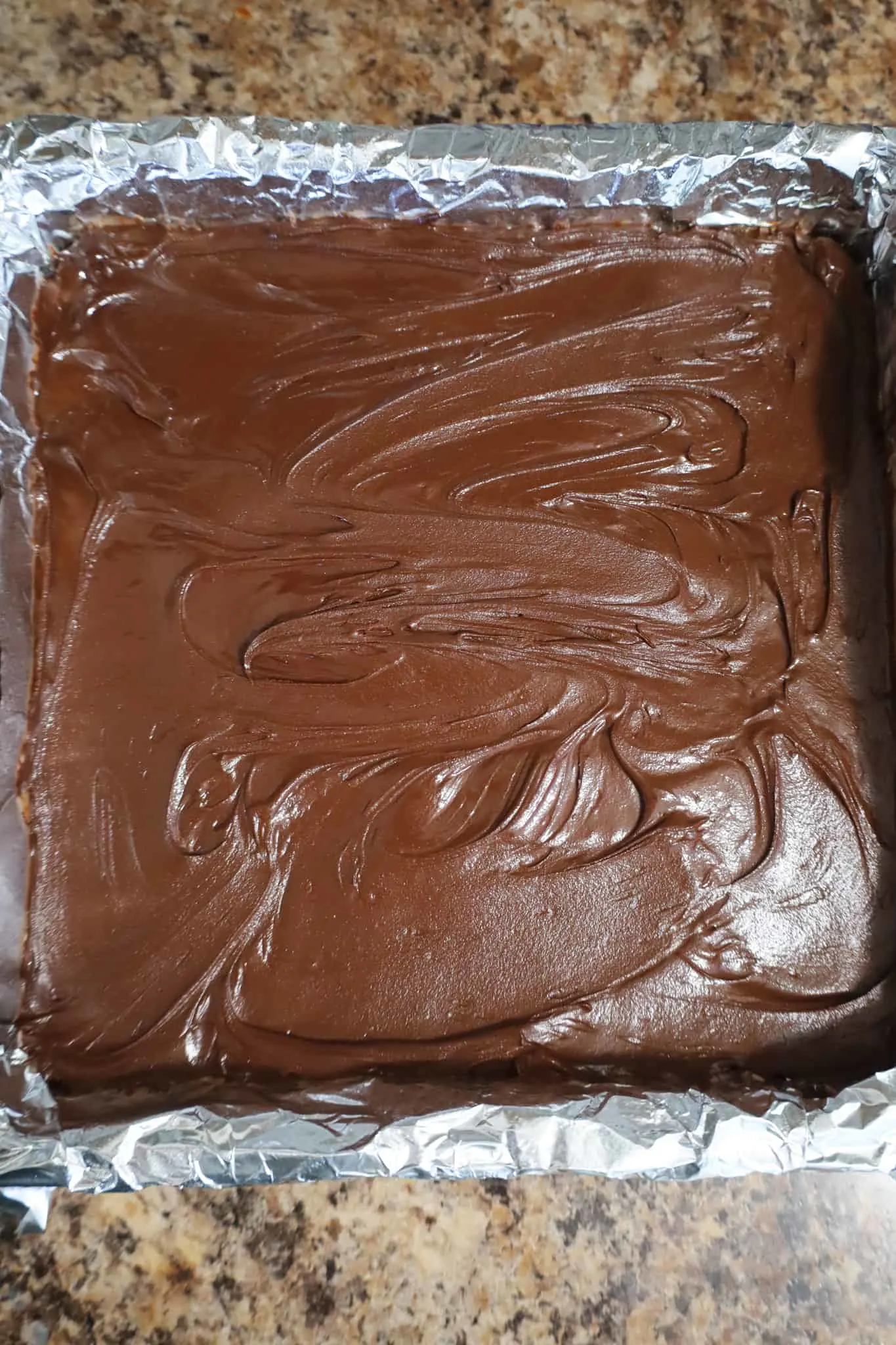melted chocolate spread on top of peanut butter bars in a baking pan