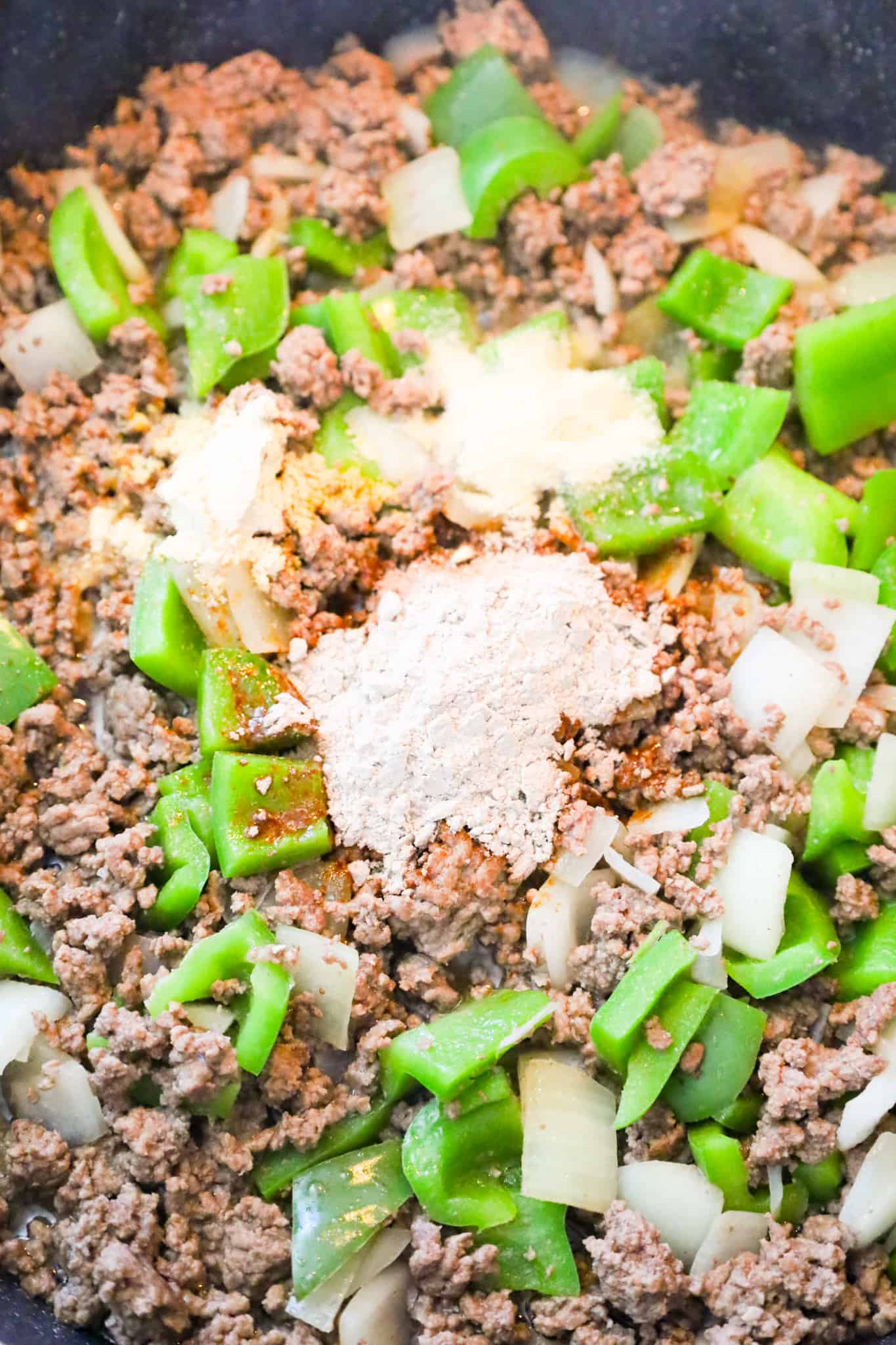 gravy mix and spices on top of cooked ground beef, peppers and onions in a saute pan