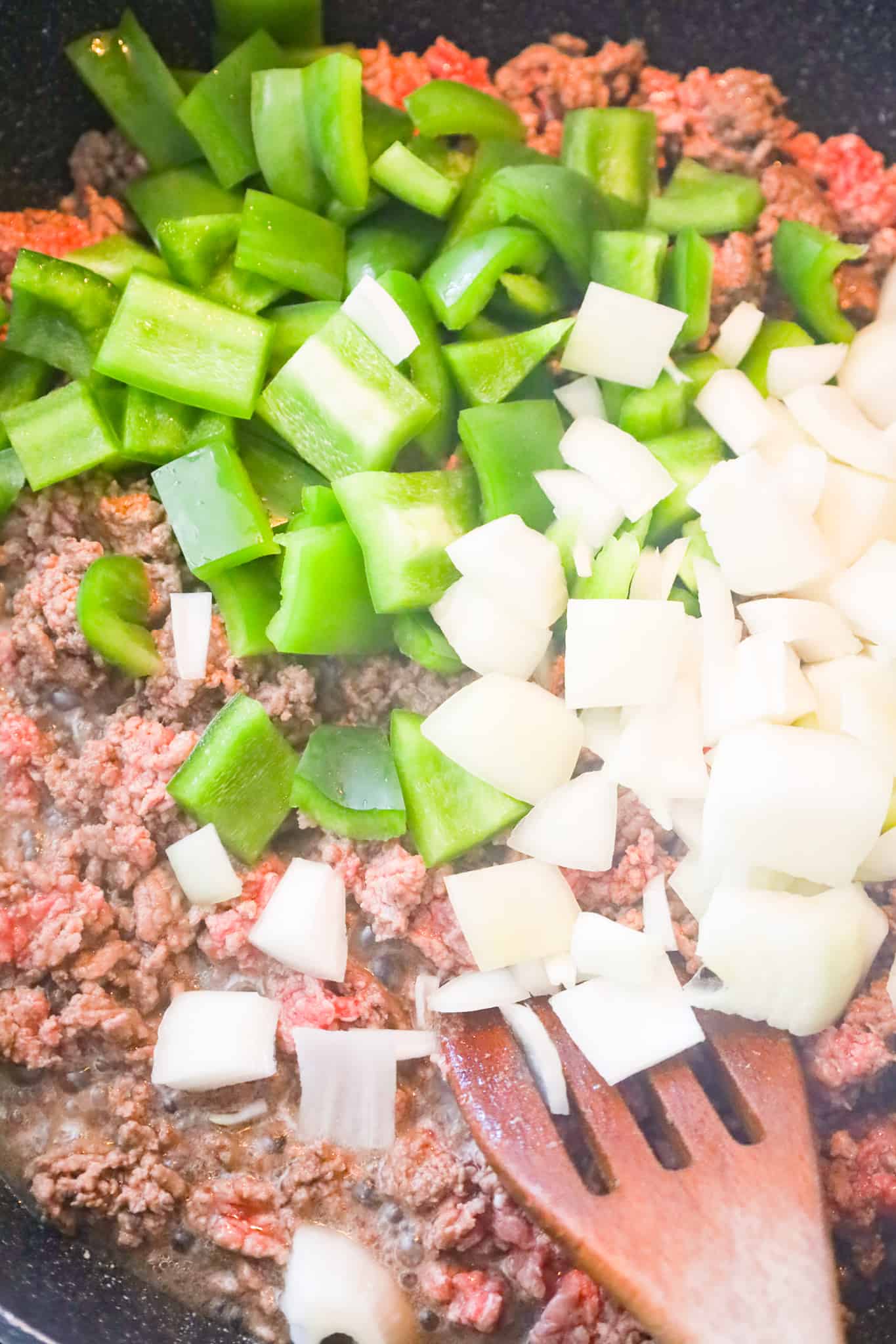 diced onions and diced green peppers on top of ground beef in a saute pan