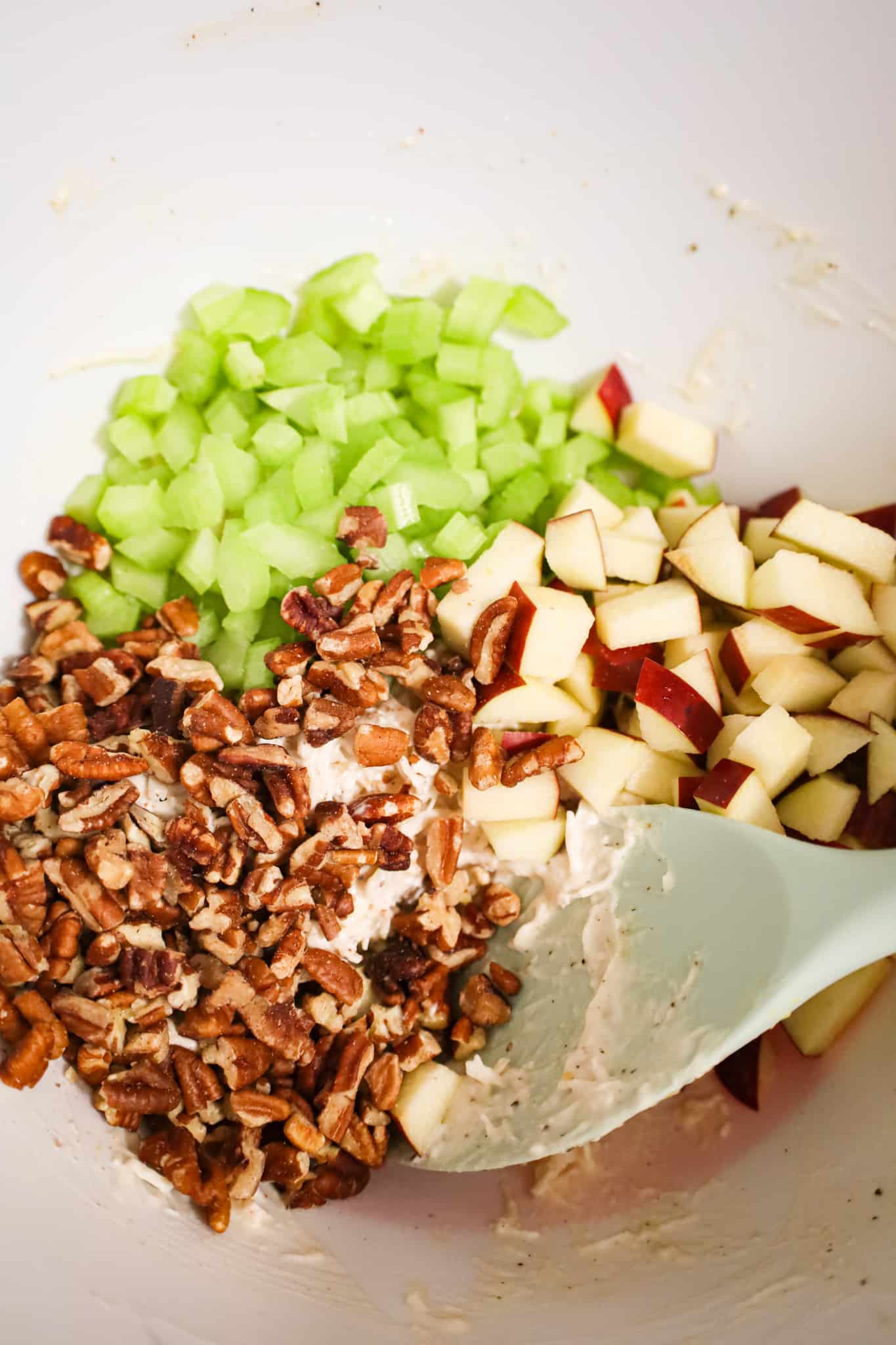 pecan pieces, diced celery and diced apples on top of shredded chicken and mayo mixture in a mixing bowl