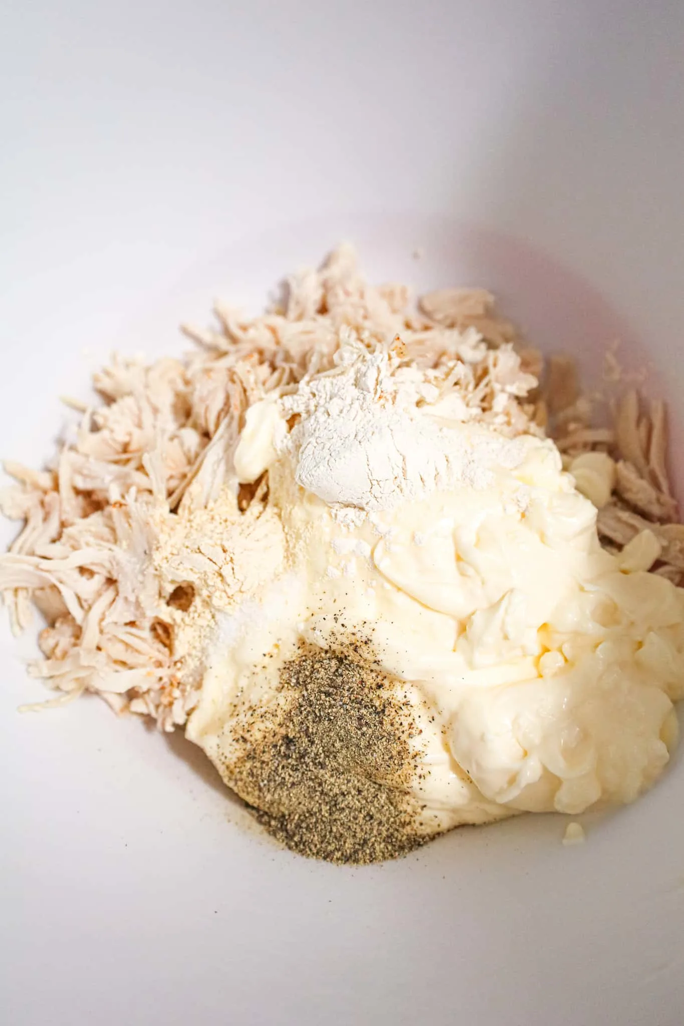 spices on top of mayo and shredded chicken in a mixing bowl