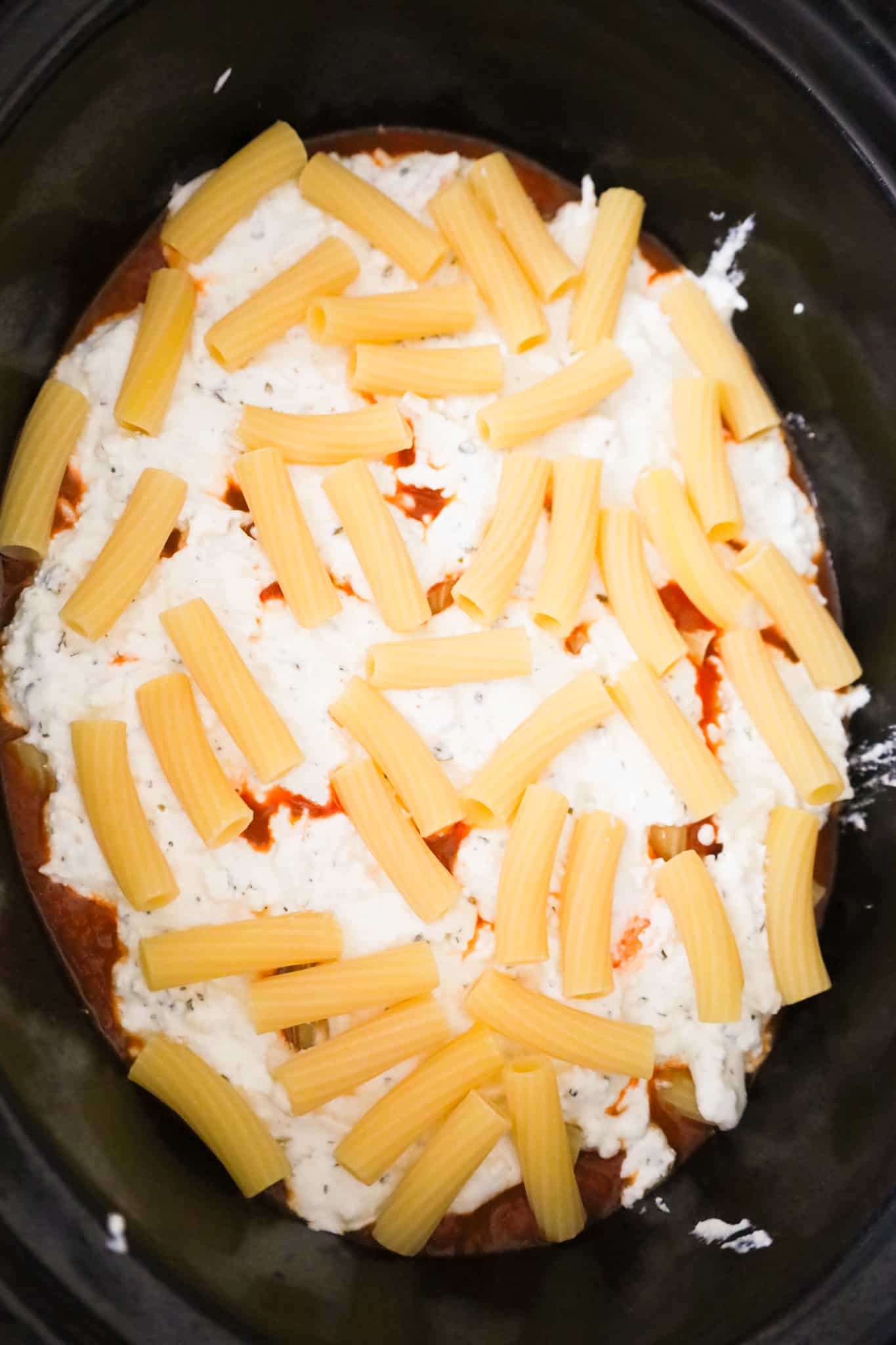 uncooked noodles on top of ricotta mixture and marinara in a slow cooker